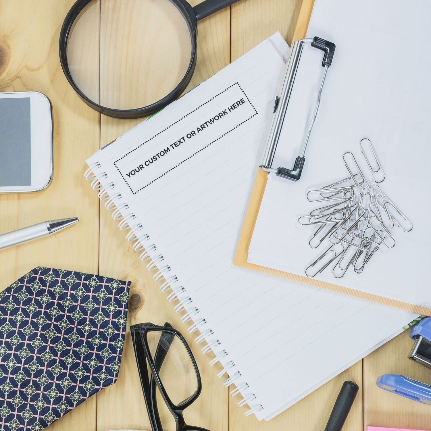 Desk with office supplies, including a notebook stamped with YOUR CUSTOM TEXT OR ARTWORK HERE using a Custom Rubber Stamp Size 1-1/2 x 6.