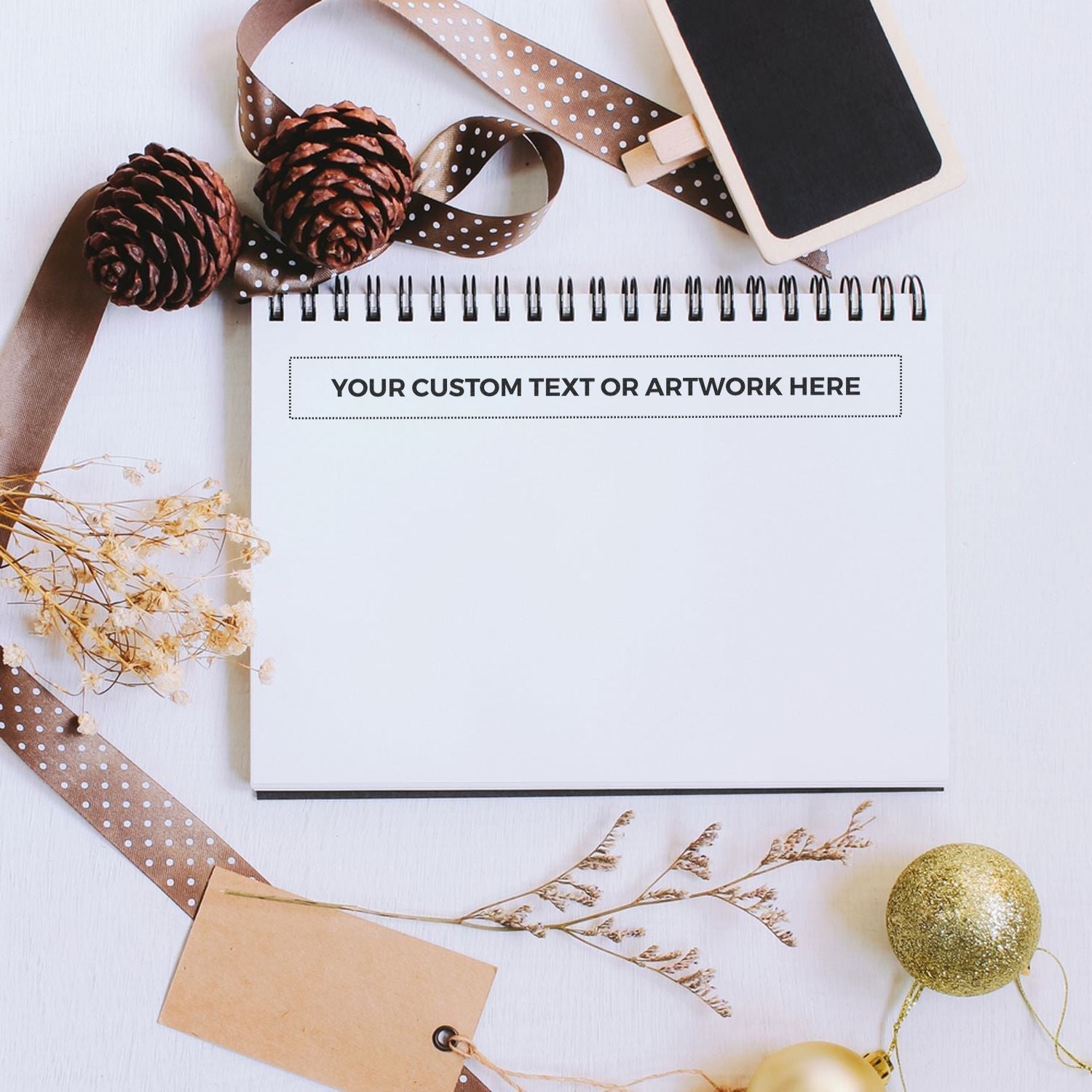 Custom Rubber Stamp Size 1 x 10 stamped on a notebook page, surrounded by pinecones, ribbon, dried flowers, and holiday decorations.