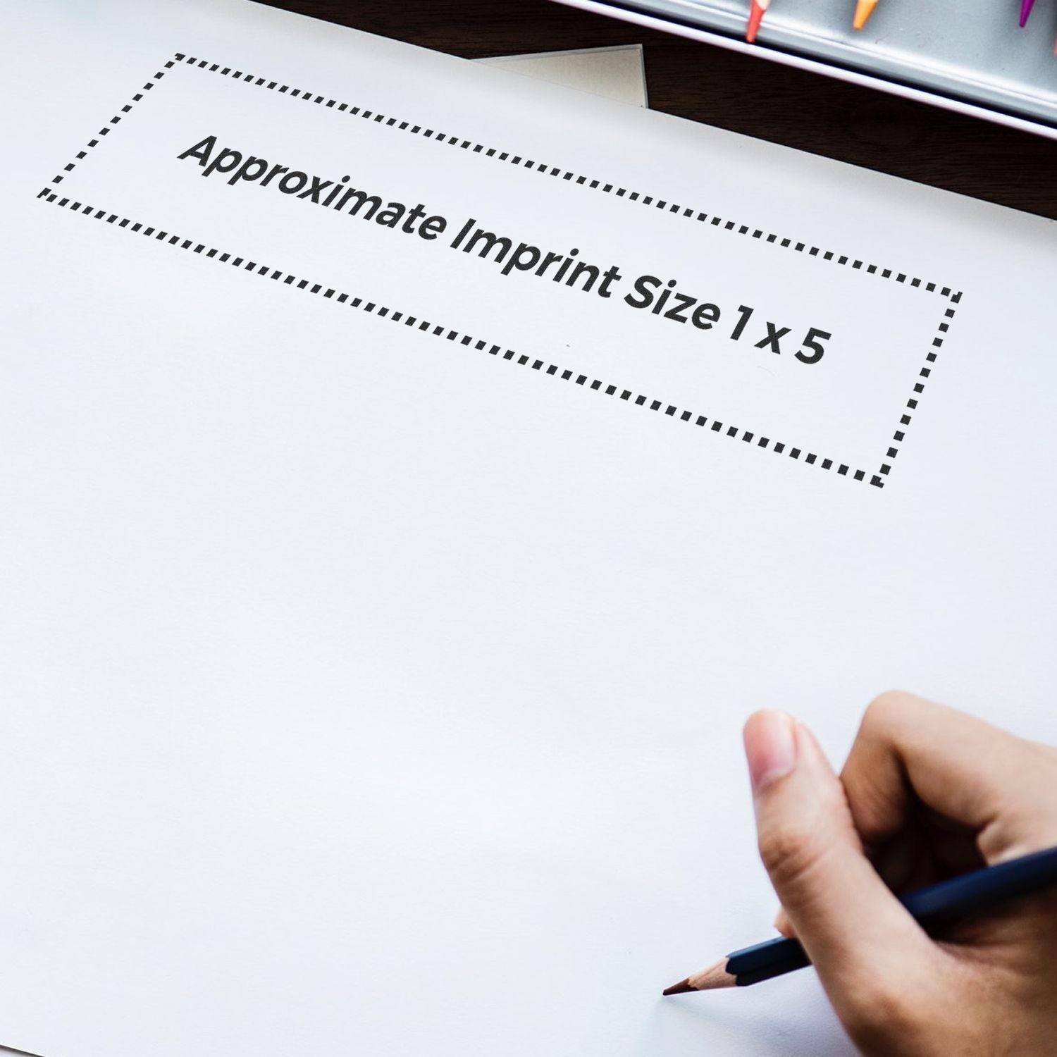 Hand holding a pen near a paper with a dotted rectangle labeled Approximate Imprint Size 1 x 5 for Custom Rubber Stamp Size 1 x 5.