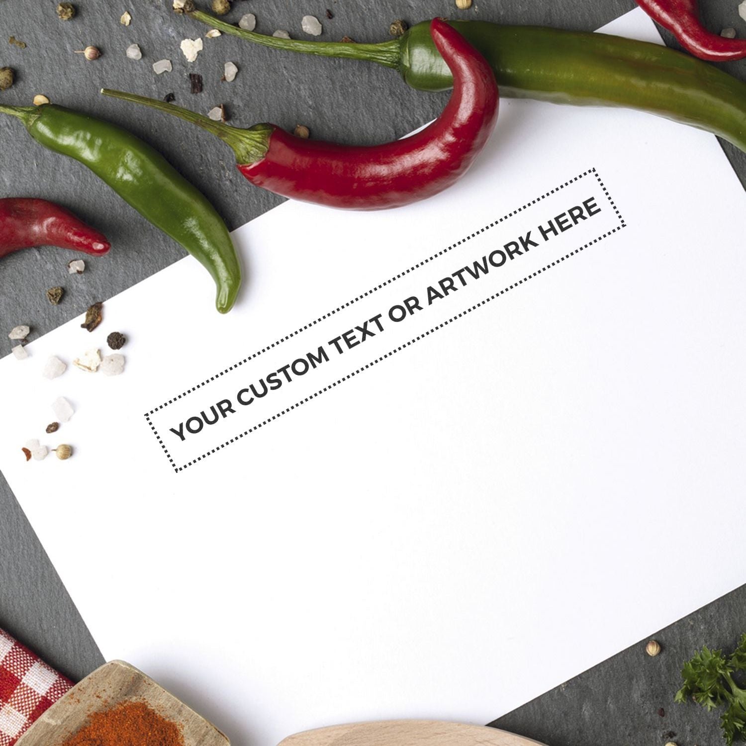 Custom Rubber Stamp Size 1 x 8 stamped on white paper, surrounded by red and green chili peppers, peppercorns, and herbs on a dark surface.