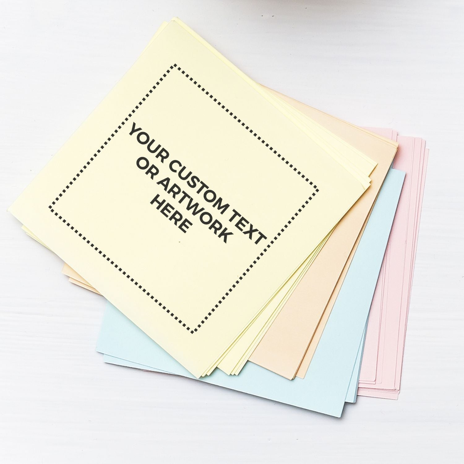 Custom Rubber Stamp Size 2 x 2 used on a stack of pastel-colored papers with Your Custom Text or Artwork Here stamped in black.