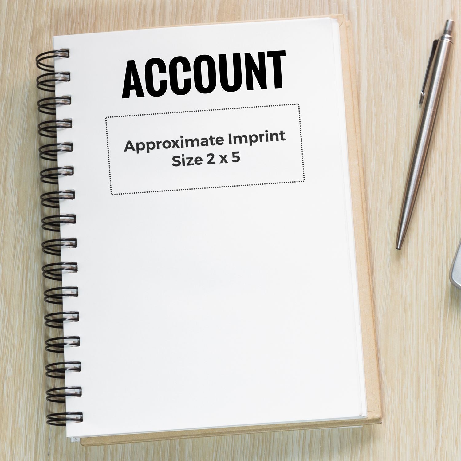 Custom Rubber Stamp Size 2 x 5 imprint on a spiral notebook with ACCOUNT text, pen beside it on a wooden surface.