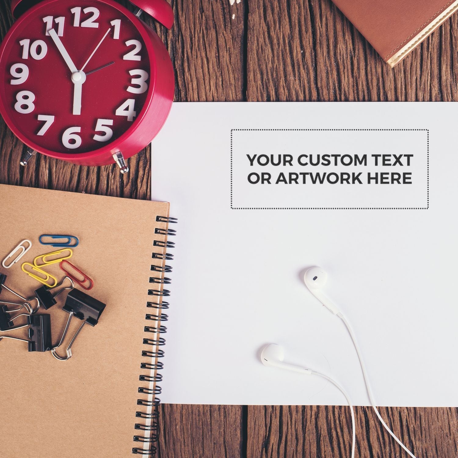 Custom Rubber Stamp Size 2 x 5 stamped on white paper, surrounded by a red clock, notebook, paper clips, and earphones on a wooden desk.