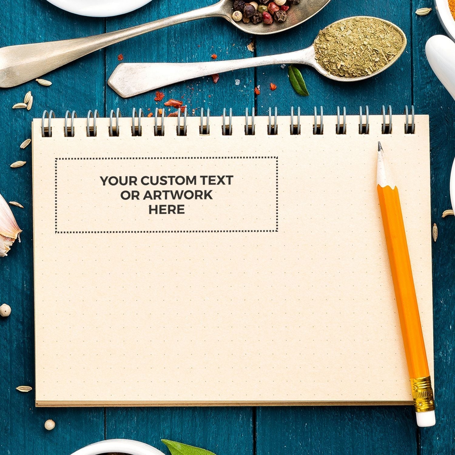 Custom Rubber Stamp Size 2 x 6 stamped on a spiral notebook page with a pencil, surrounded by spices and kitchen utensils on a blue wooden table.