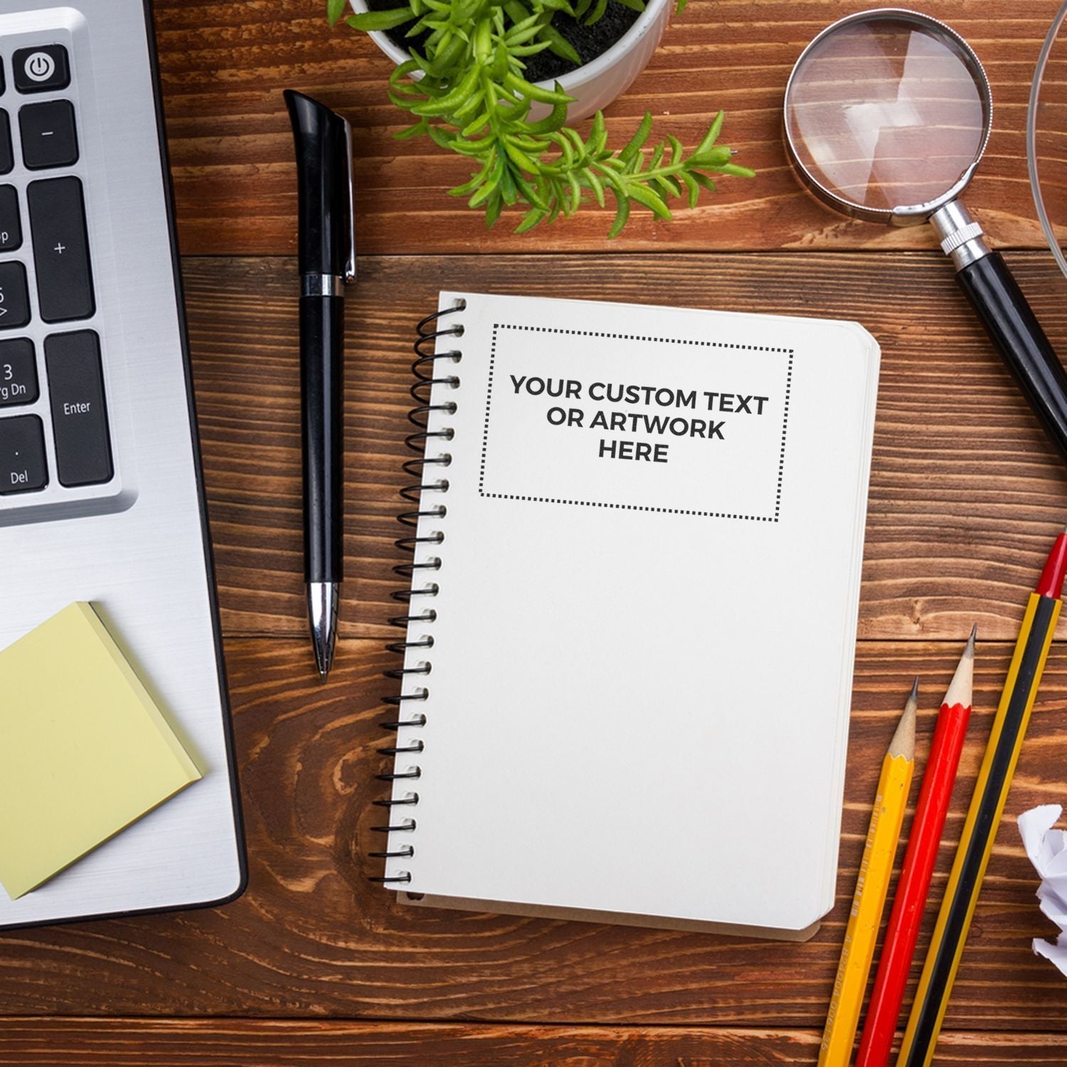 Custom Rubber Stamp Size 4 x 7 used on a spiral notebook with text YOUR CUSTOM TEXT OR ARTWORK HERE on a wooden desk with office supplies.