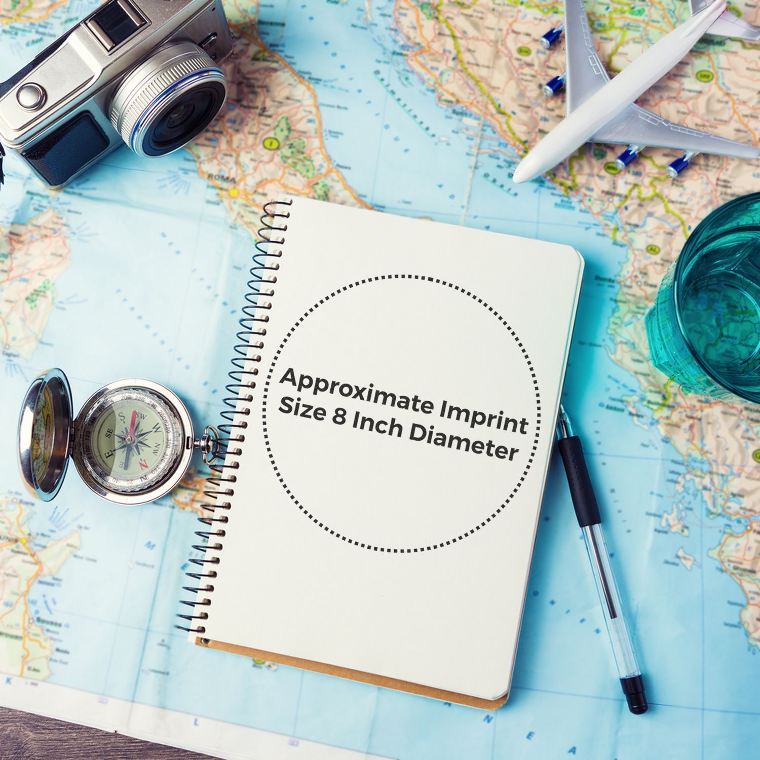 Notebook with Approximate Imprint Size 8 Inch Diameter text, surrounded by a camera, compass, pen, airplane model, and map. Custom Rubber Stamp Size 8 Inch Diameter.