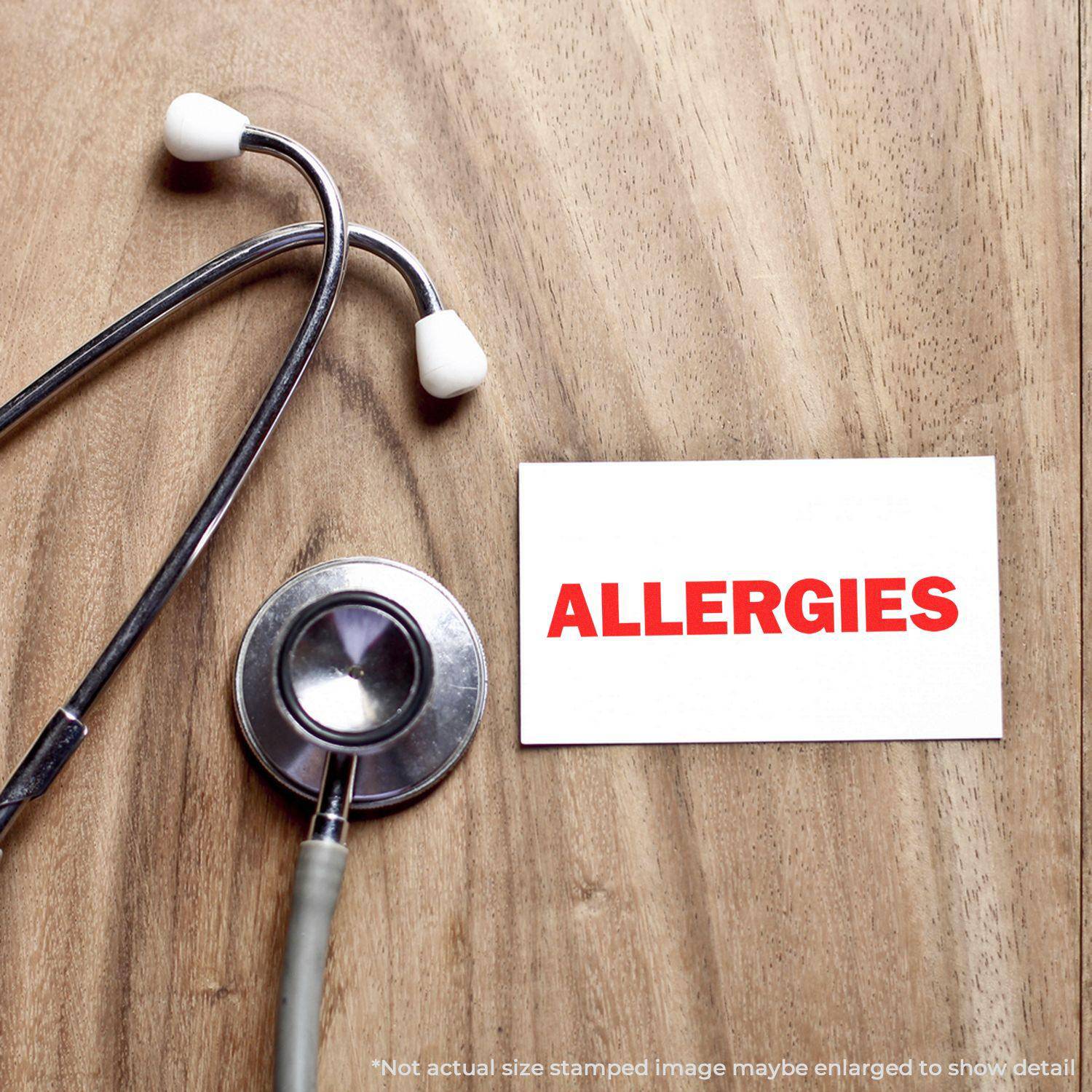 Large Pre-Inked Allergies Stamp used on a white card next to a stethoscope on a wooden surface.
