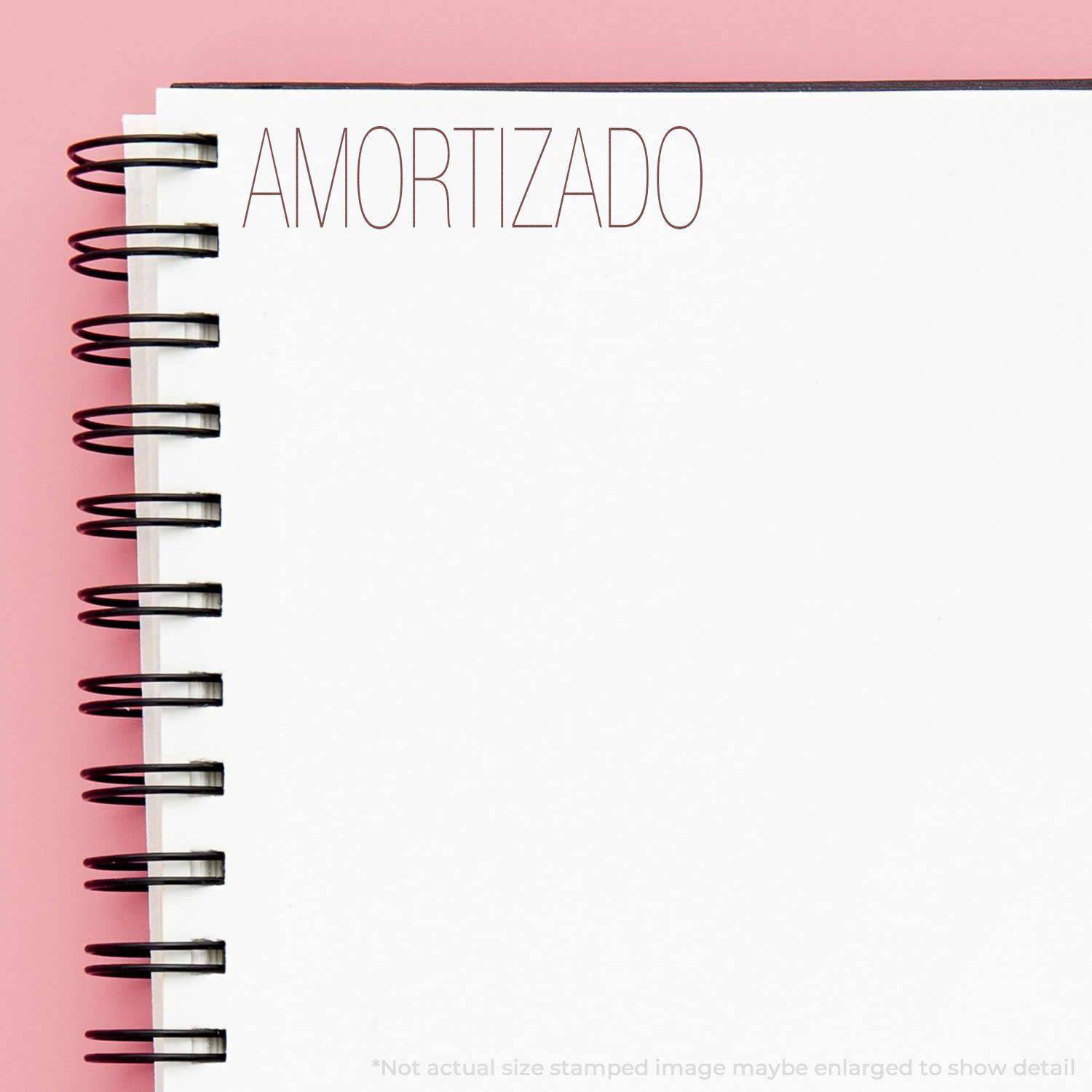 Large Pre-Inked Amortizado Stamp used on a white spiral notebook with a pink background. The word AMORTIZADO is stamped in red ink.