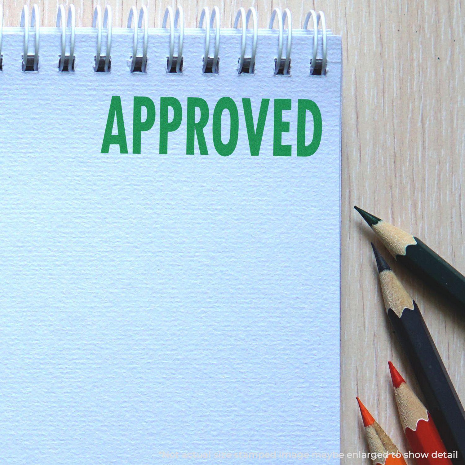 Slim Pre-Inked Approved Stamp marking APPROVED in green on a spiral notebook, with colored pencils beside it.