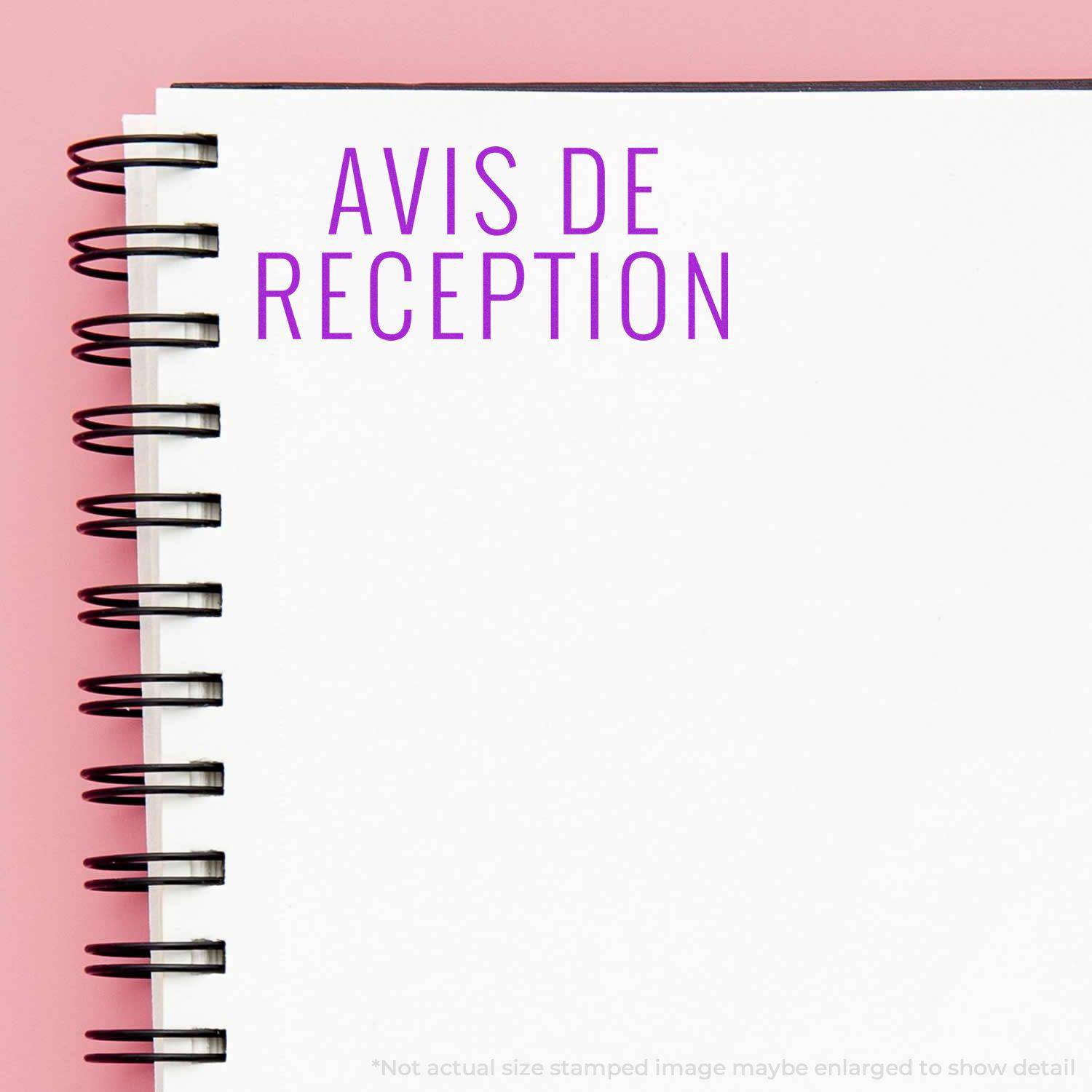 Large Pre-Inked Avis De Reception Stamp used on a white spiral notebook with a pink background.