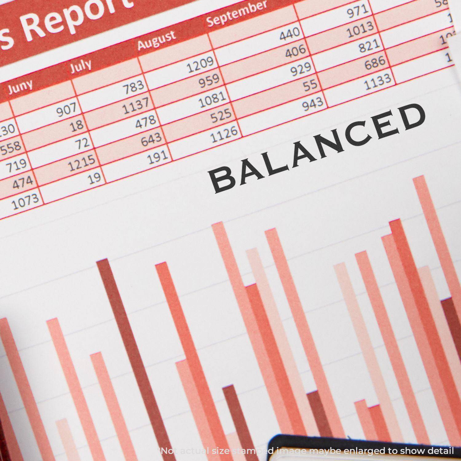 A Large Pre-Inked Balanced Stamp is used on a financial report with bar graphs and a table, stamping the word BALANCED in bold black letters.