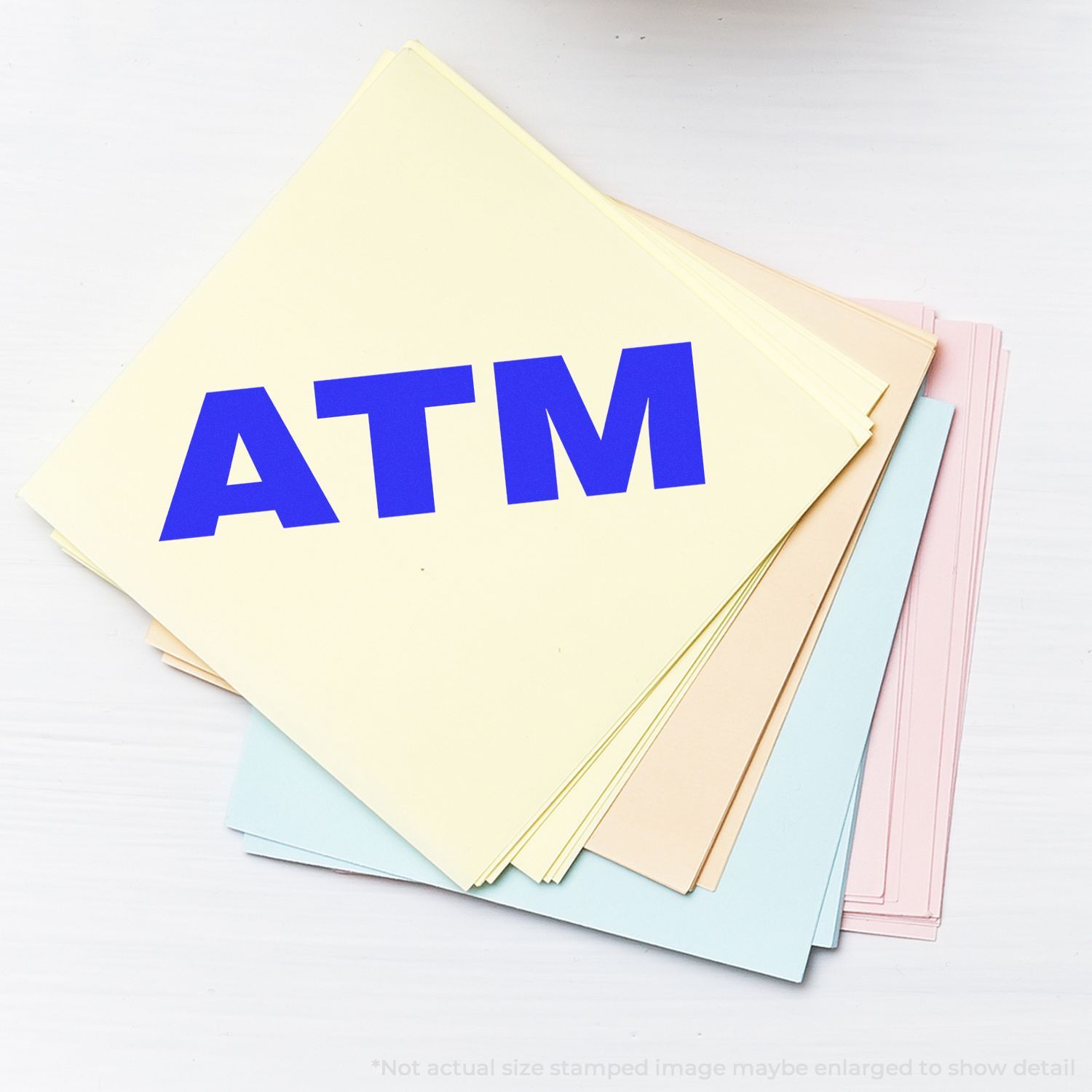 Large Pre Inked ATM Stamp on a stack of pastel-colored papers with a bold blue ATM imprint.