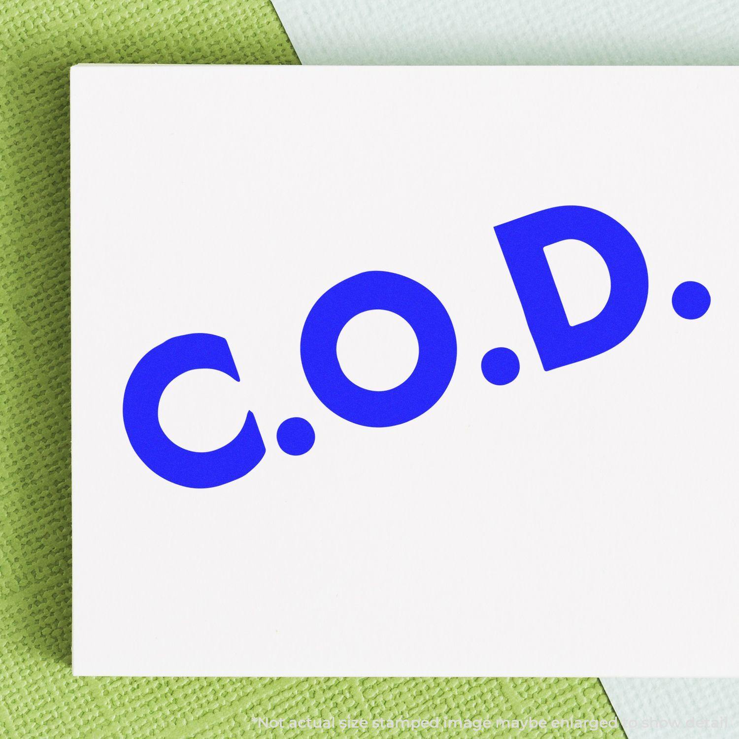 Self Inking Bold COD Stamp imprinting C.O.D. in blue ink on white paper, placed on a green textured surface.