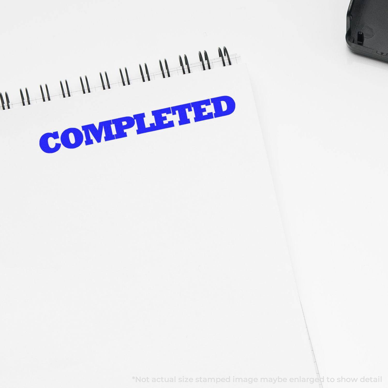 Large Self Inking Bold Completed Stamp in blue ink on a white spiral notebook, showing the word COMPLETED clearly stamped.