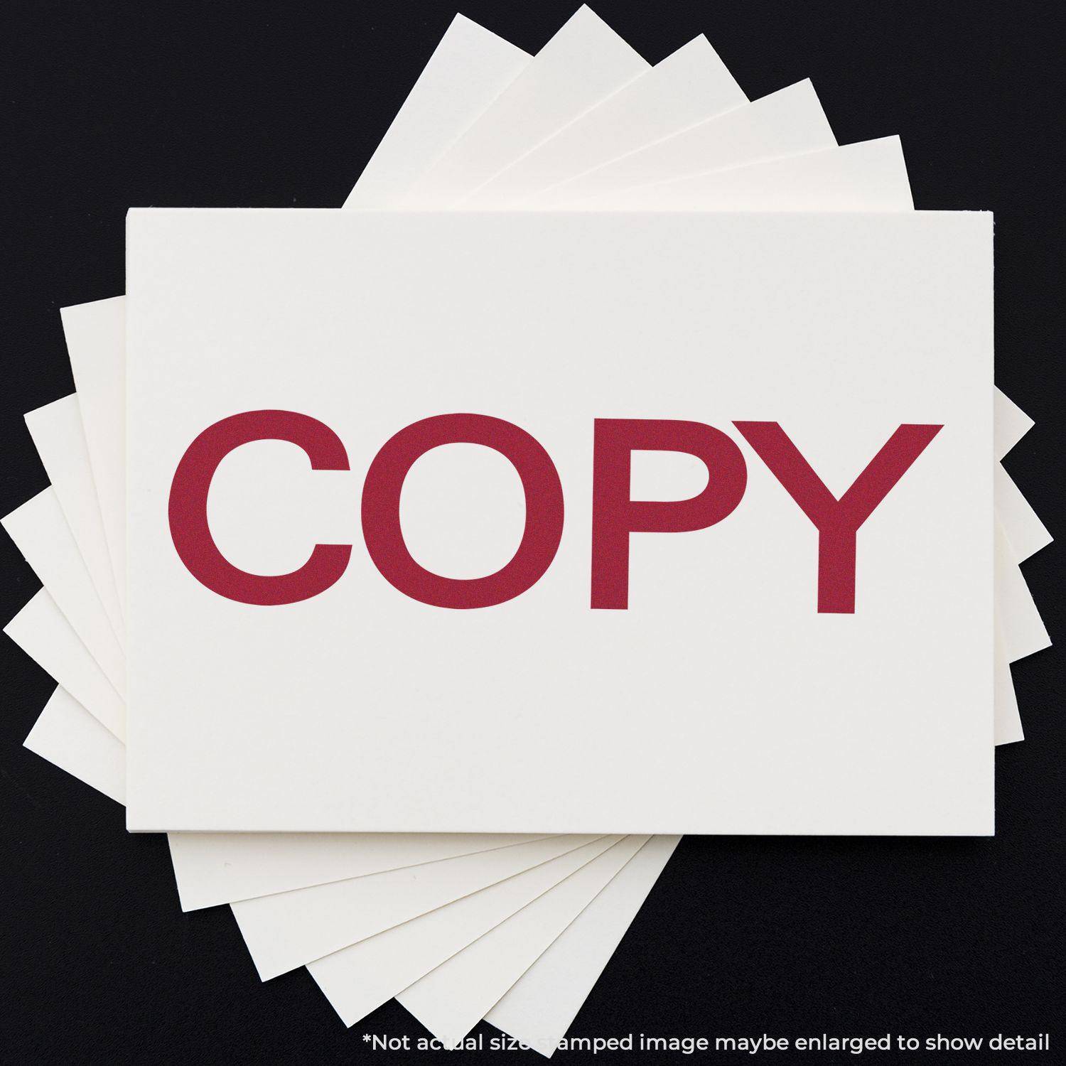 Large Self Inking Bold Copy Stamp marking COPY in red on white paper, with multiple sheets stacked underneath on a black background.
