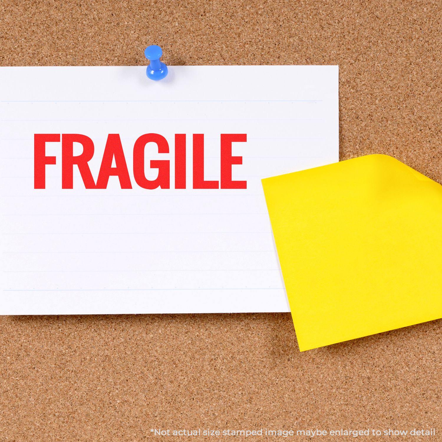 A corkboard with a note pinned by a blue pushpin reading FRAGILE in red, stamped by a Slim Pre-Inked Bold Fragile Stamp.
