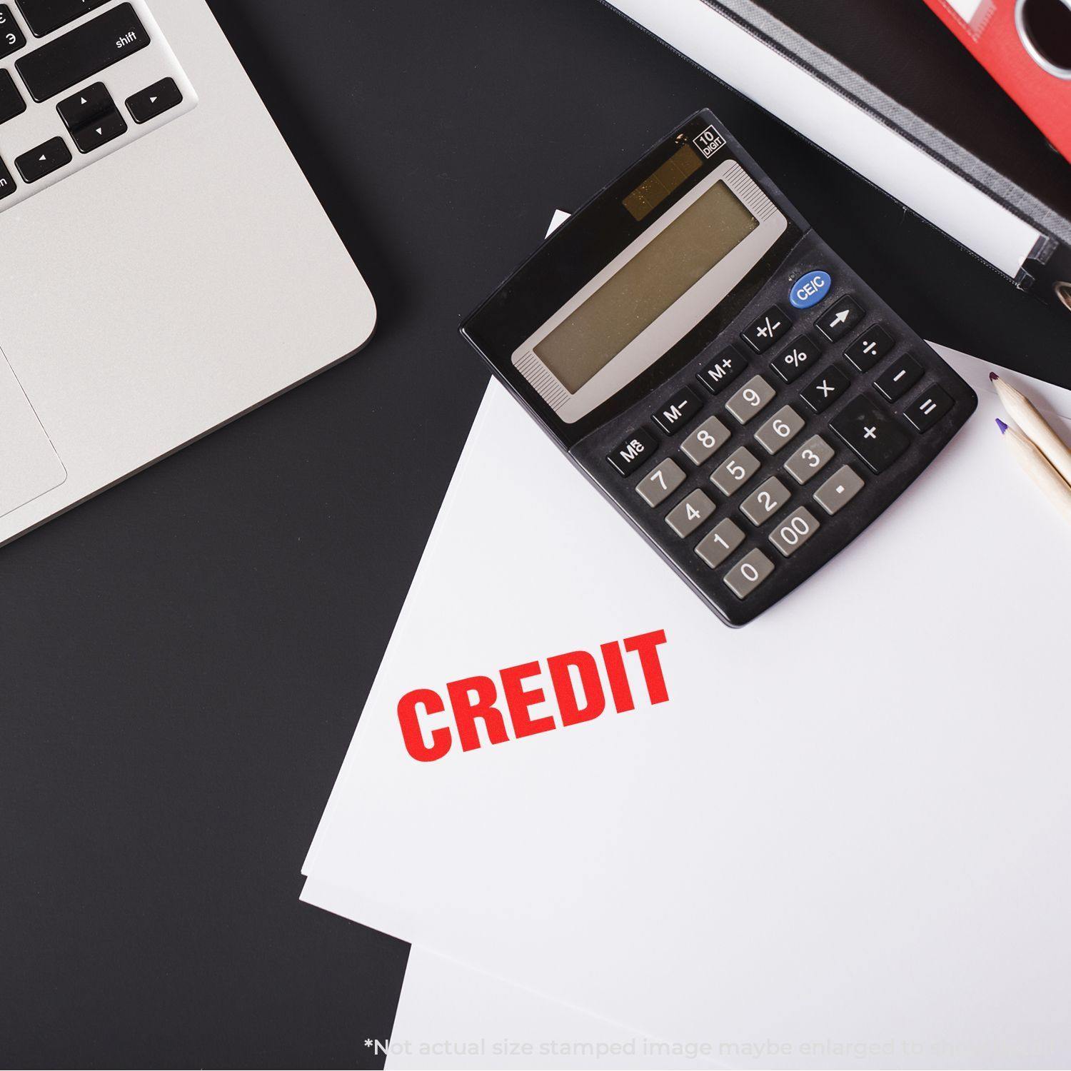 Large Credit Self-Inking Stamp in bold red on white paper, next to a calculator, pencil, and laptop on a black desk.