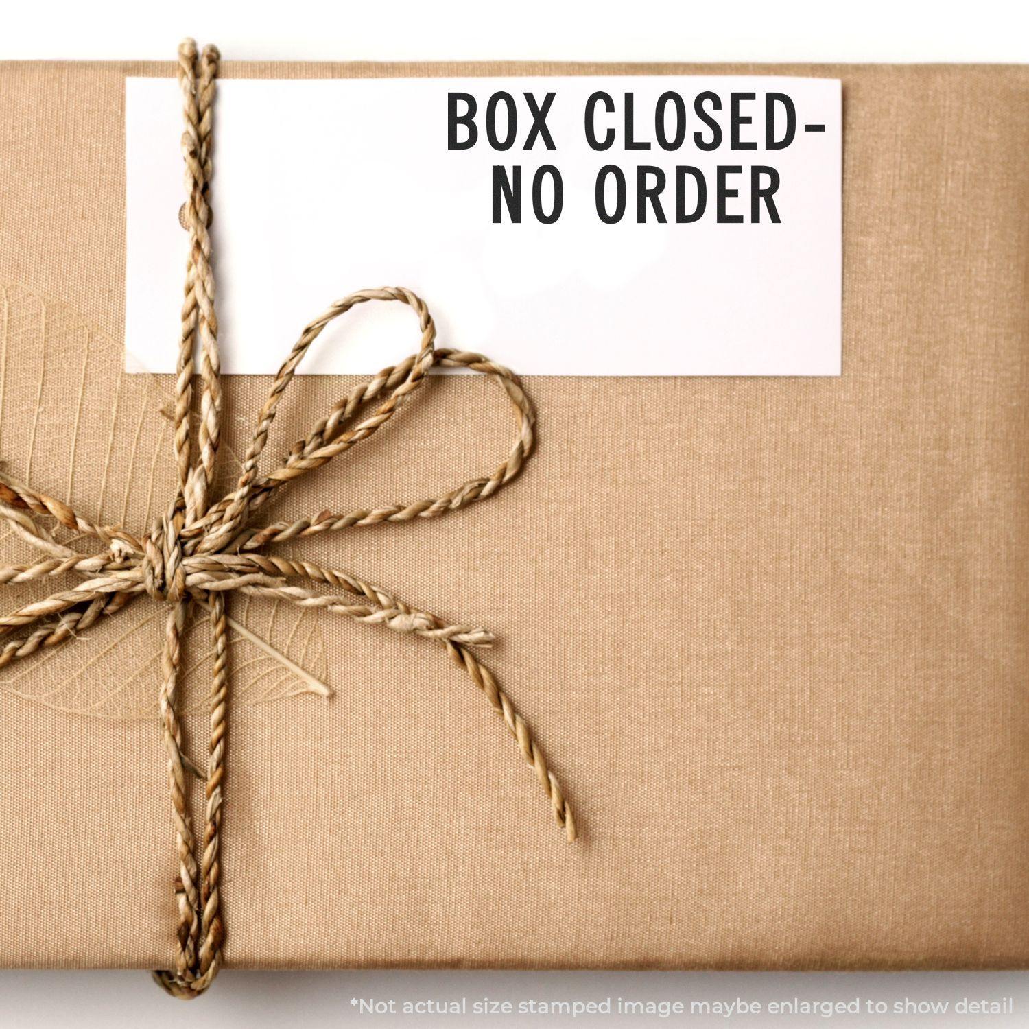 A brown paper-wrapped box with a twine bow and a white card displaying the text Box Closed No Order Rubber Stamp.