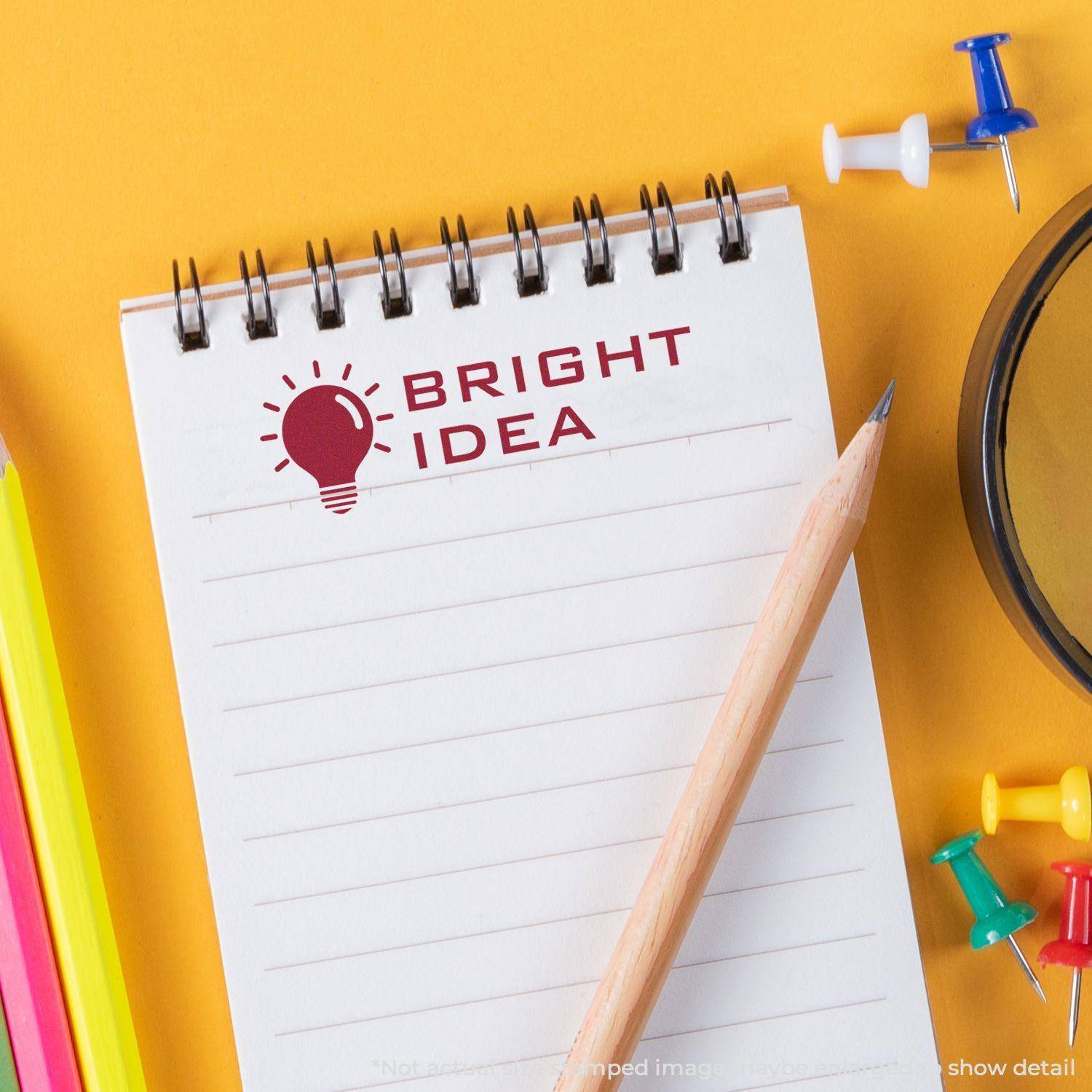 A notebook stamped with Bright Idea using the Large Self Inking Bright Idea Stamp, surrounded by colorful pencils, push pins, and a pencil.
