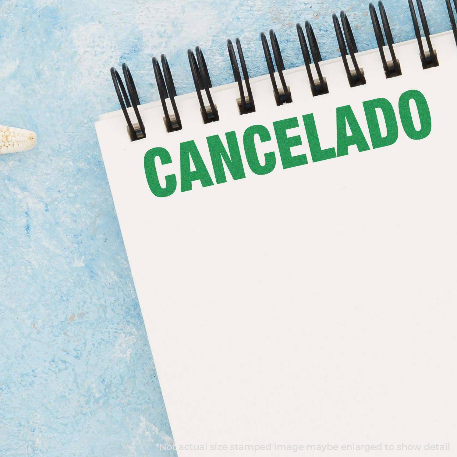 A Large Self Inking Cancelado Stamp is used on a white notepad, leaving a clear green CANCELADO imprint at the top of the page. The background is a light blue textured surface.