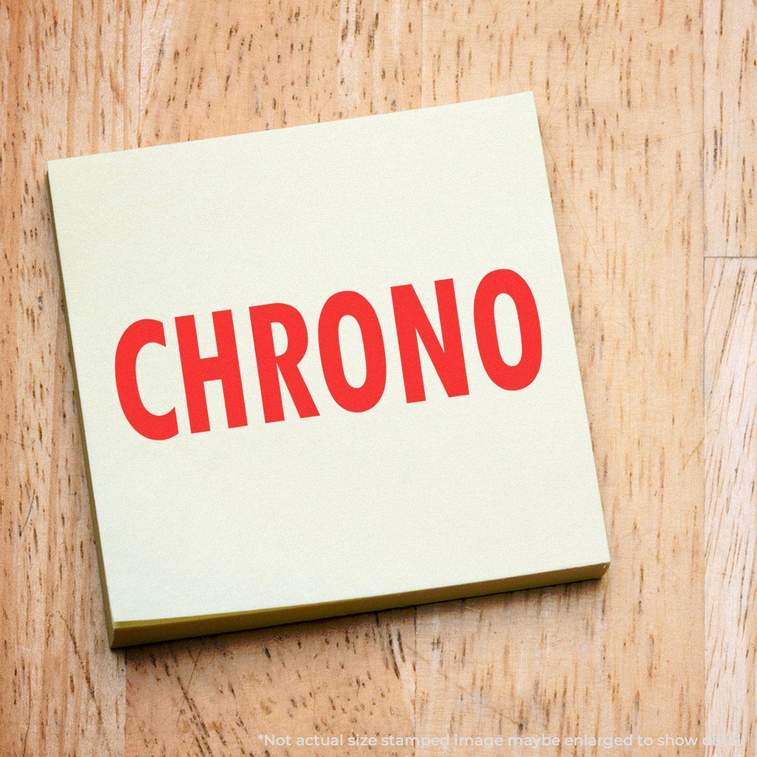 Slim Pre-Inked Chrono Stamp imprint on a yellow sticky note with the word 'CHRONO' in bold red letters on a wooden surface.