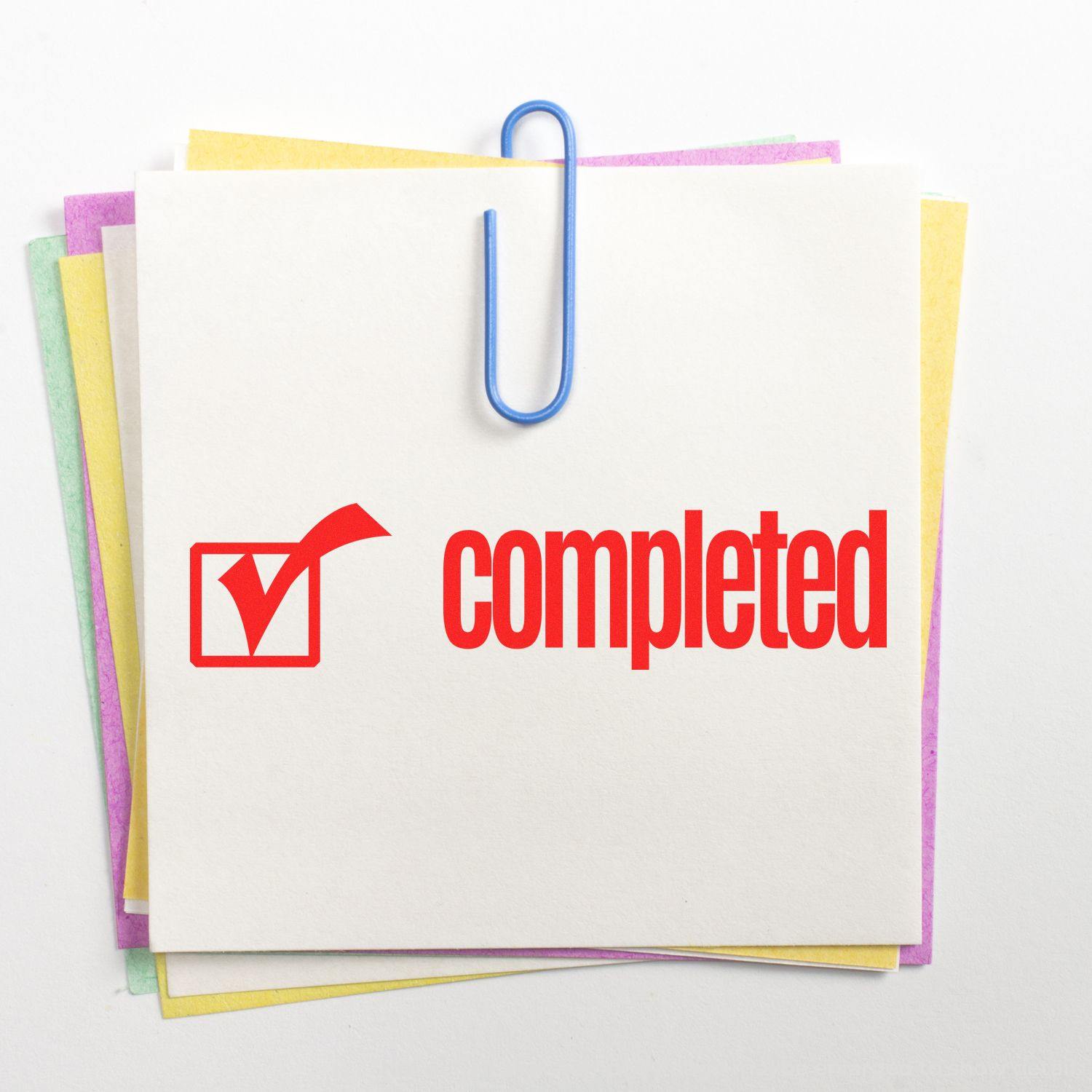 Slim Pre-Inked Completed with Checkbox Stamp on a stack of colorful sticky notes, secured with a blue paperclip.