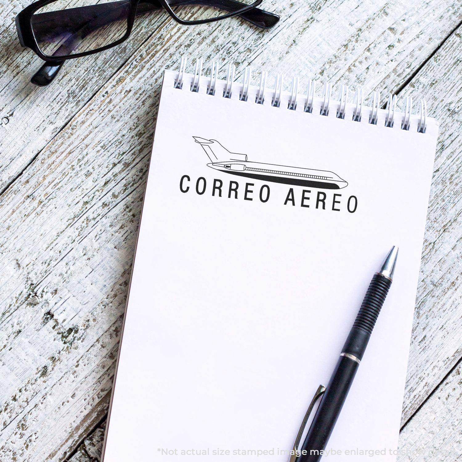 Large Pre-Inked Correo Aero Stamp used on a notepad with a pen and glasses nearby on a wooden surface.