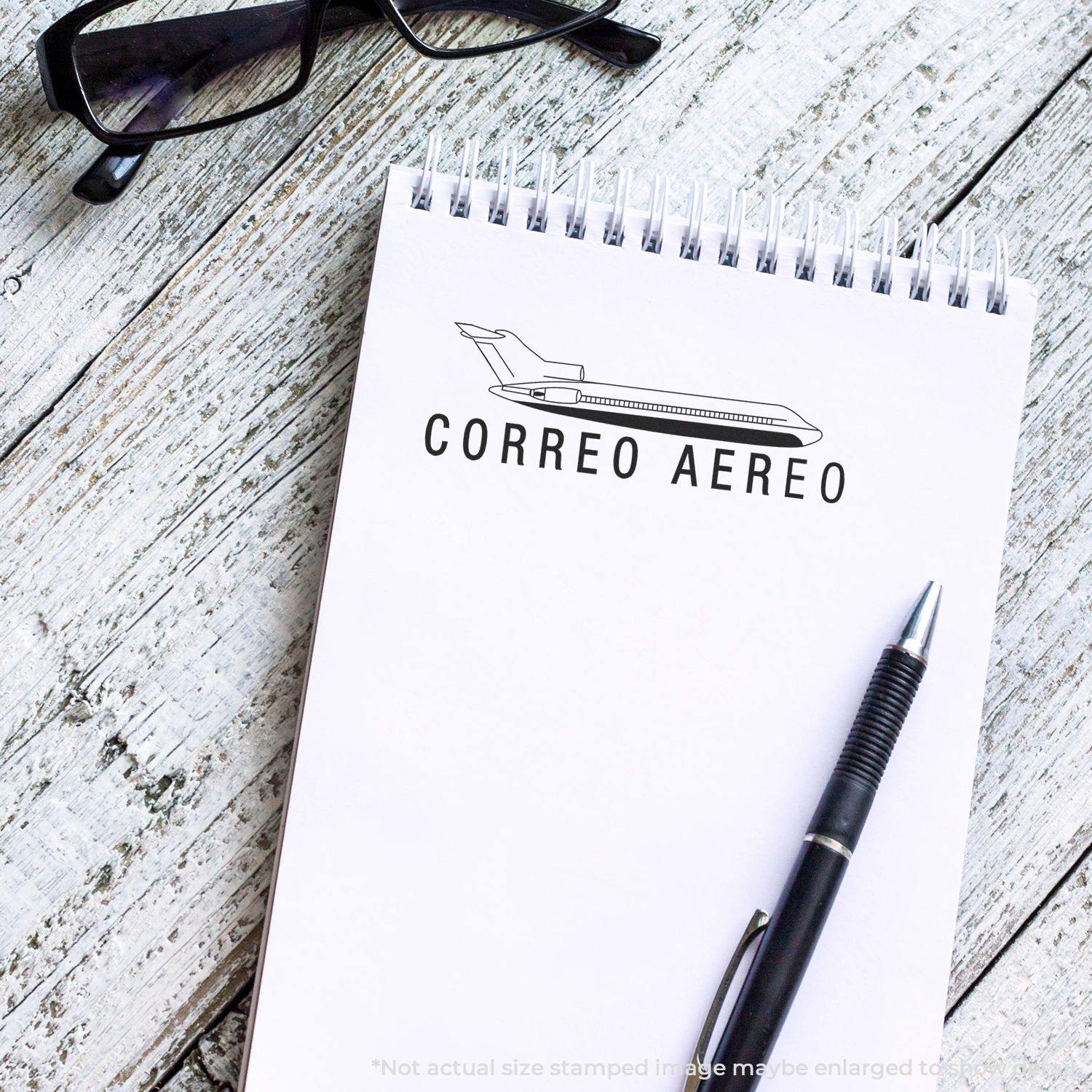Self Inking Correo Aero Stamp on a notepad with a pen and glasses on a wooden surface.