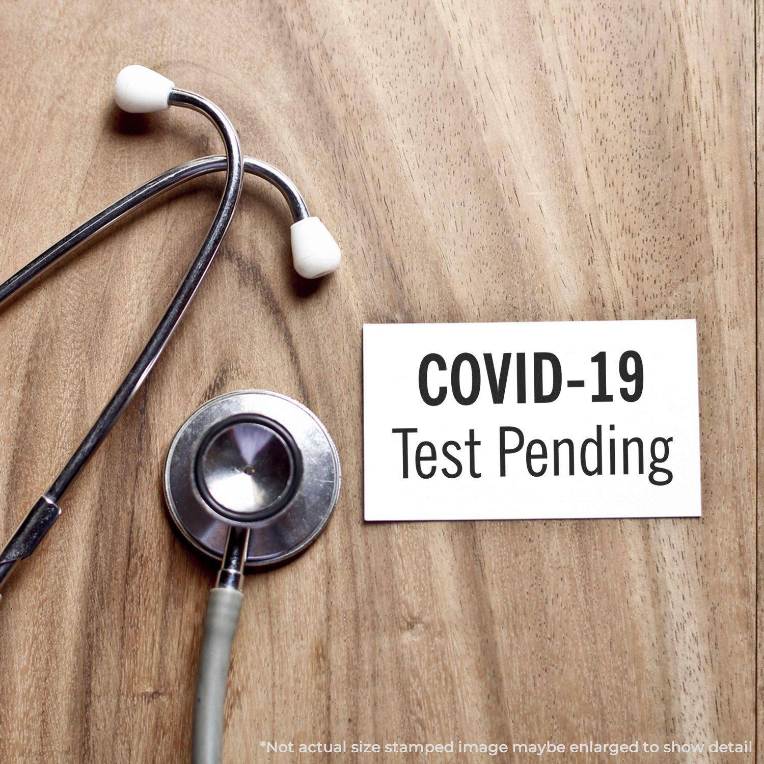 Large Pre-Inked Covid-19 Test Pending Stamp on a wooden surface next to a stethoscope, indicating a pending test result.