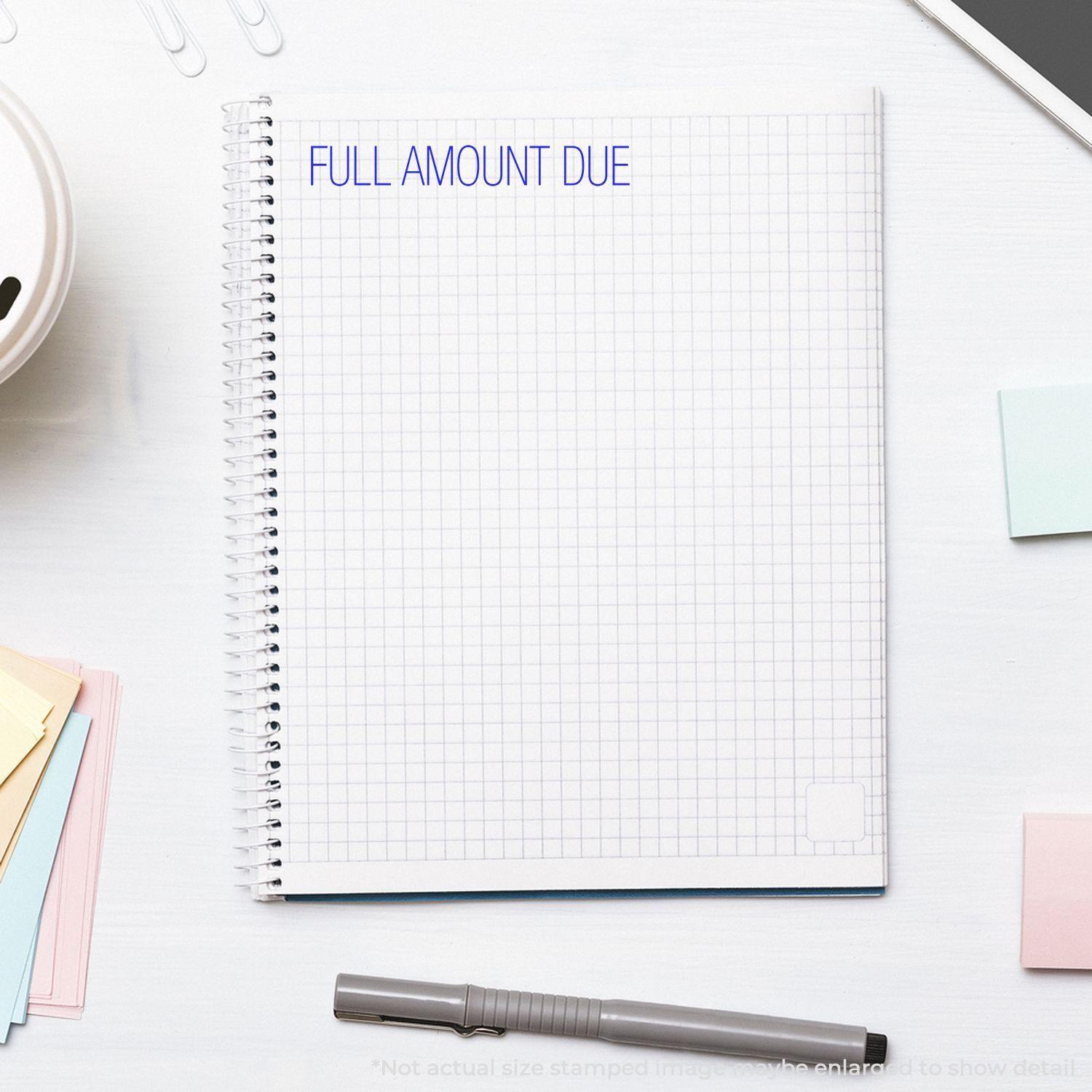 A Full Amount Due Rubber Stamp imprint on a spiral notebook with grid paper, surrounded by sticky notes, a pen, and paper clips.