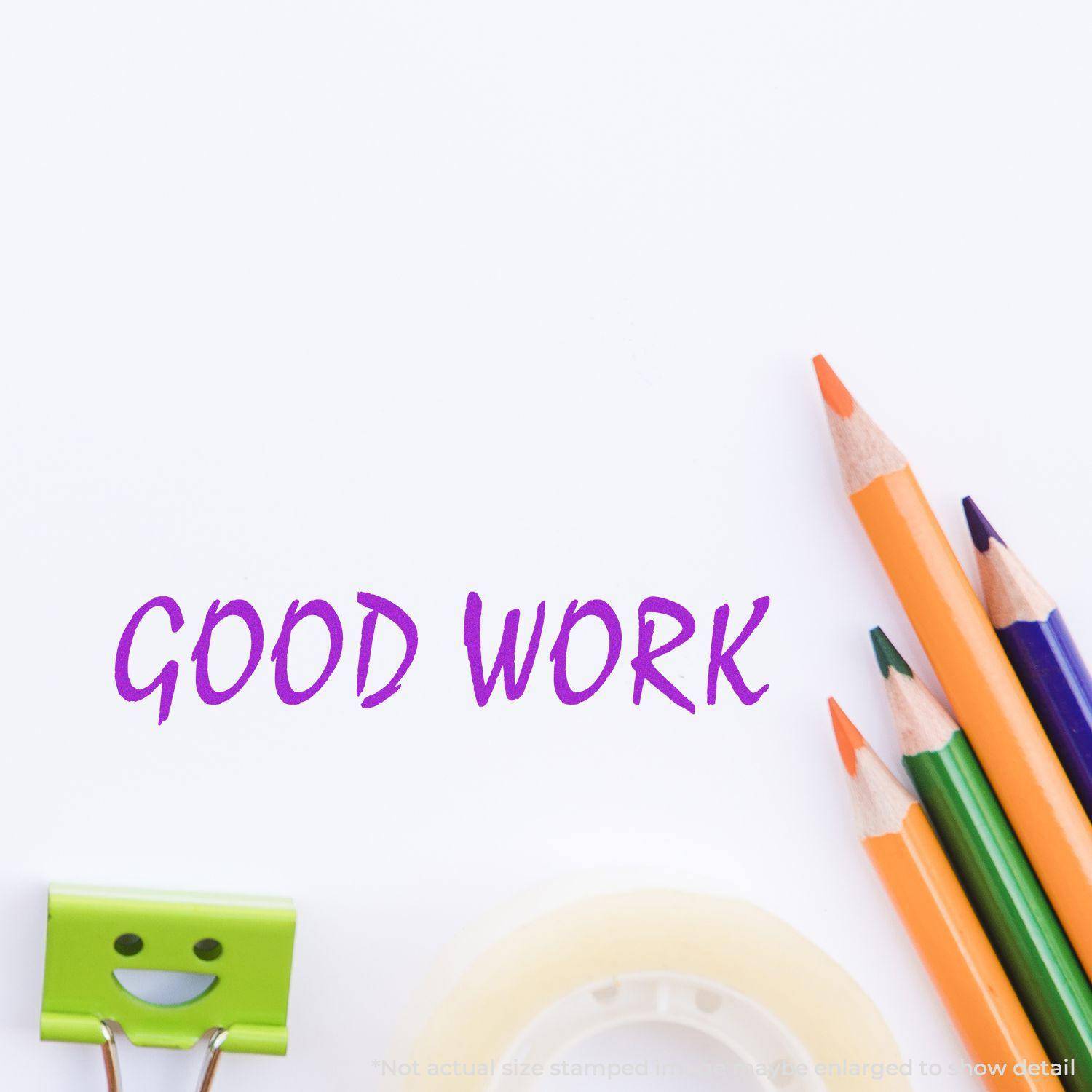Large Pre-Inked Good Work Stamp impression in purple on white paper, surrounded by colorful pencils, a smiling binder clip, and tape.