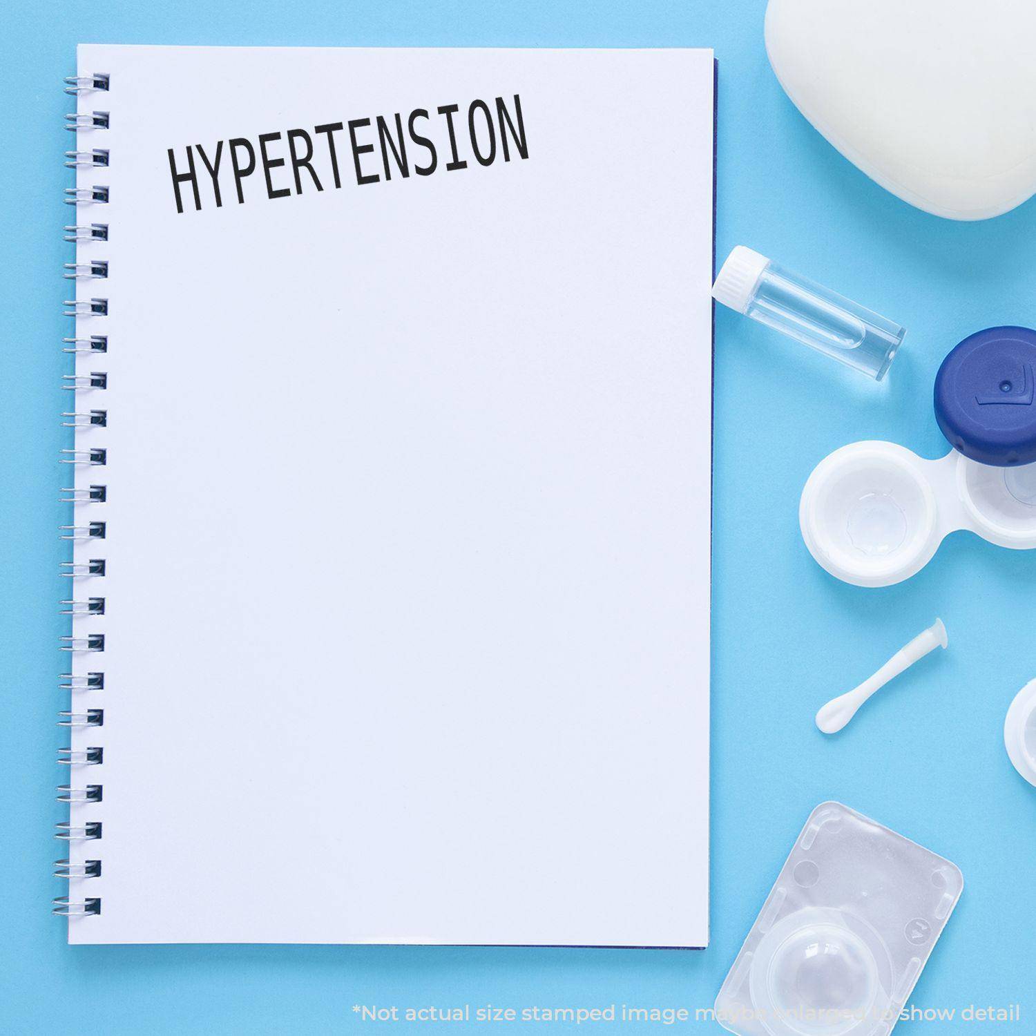 A notebook stamped with HYPERTENSION using the Large Pre-Inked Hypertension Stamp, surrounded by medical supplies on a blue background.