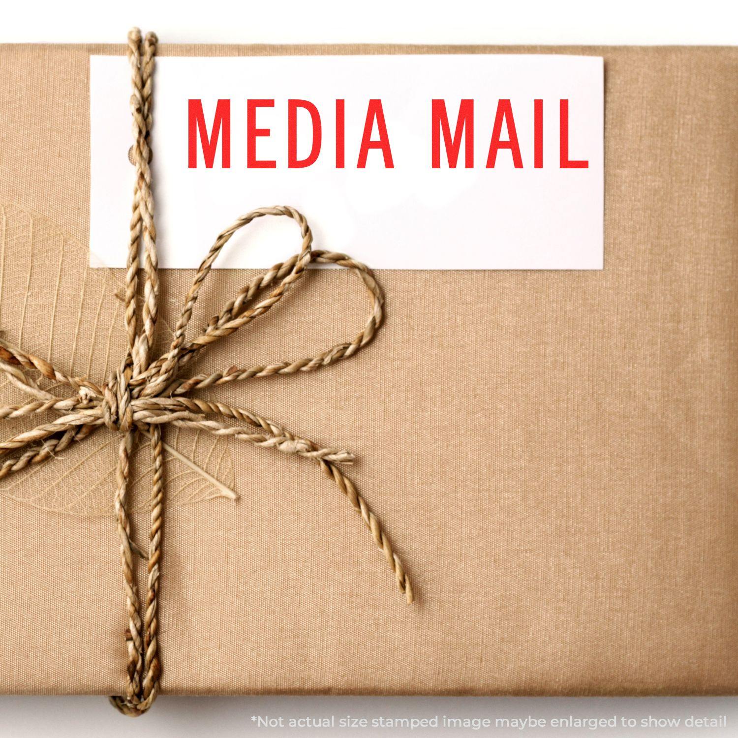 A brown package tied with twine, labeled with a Media Mail Rubber Stamp in red text.