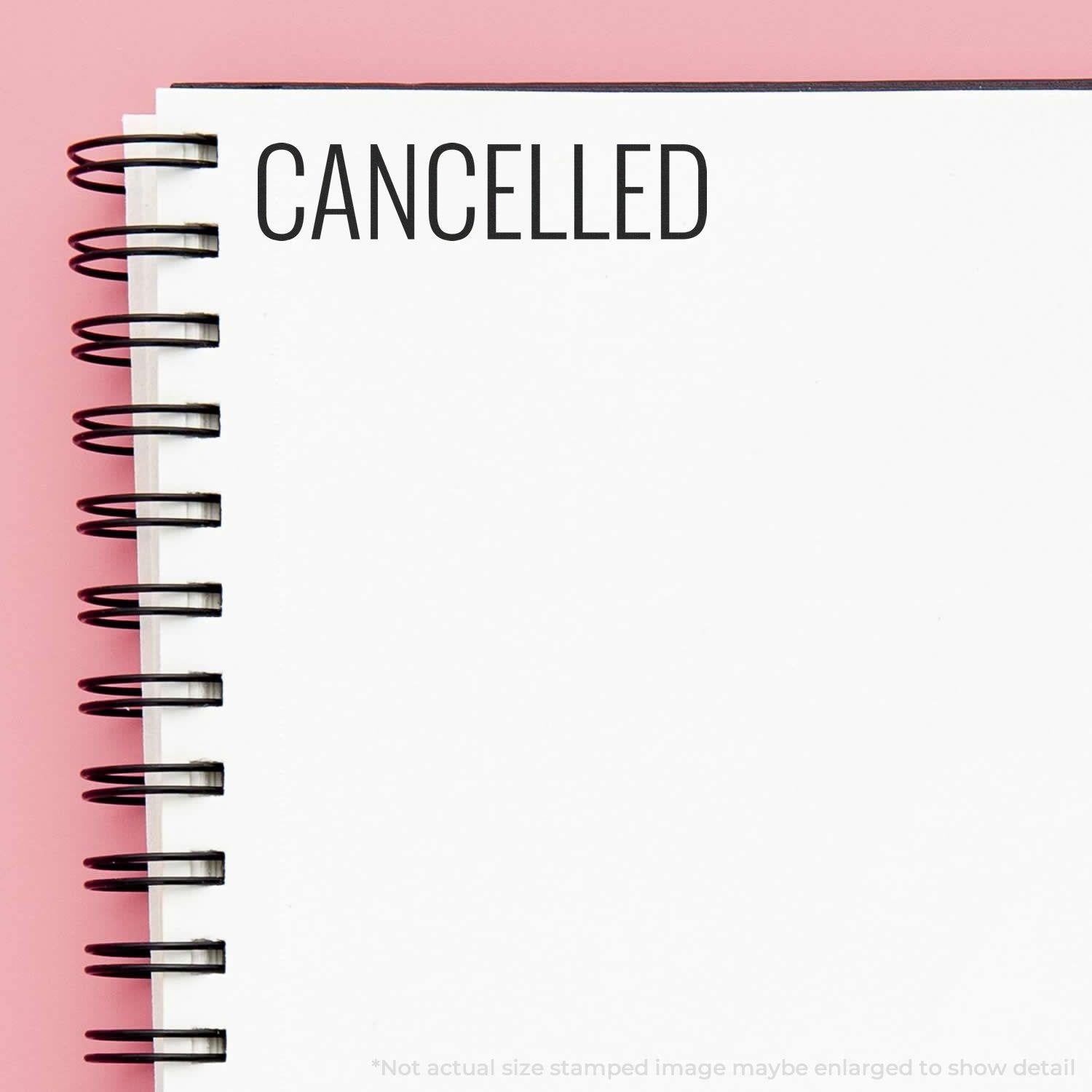 Large Self Inking Narrow Font Cancelled Stamp marking CANCELLED on a white spiral notebook with a pink background.