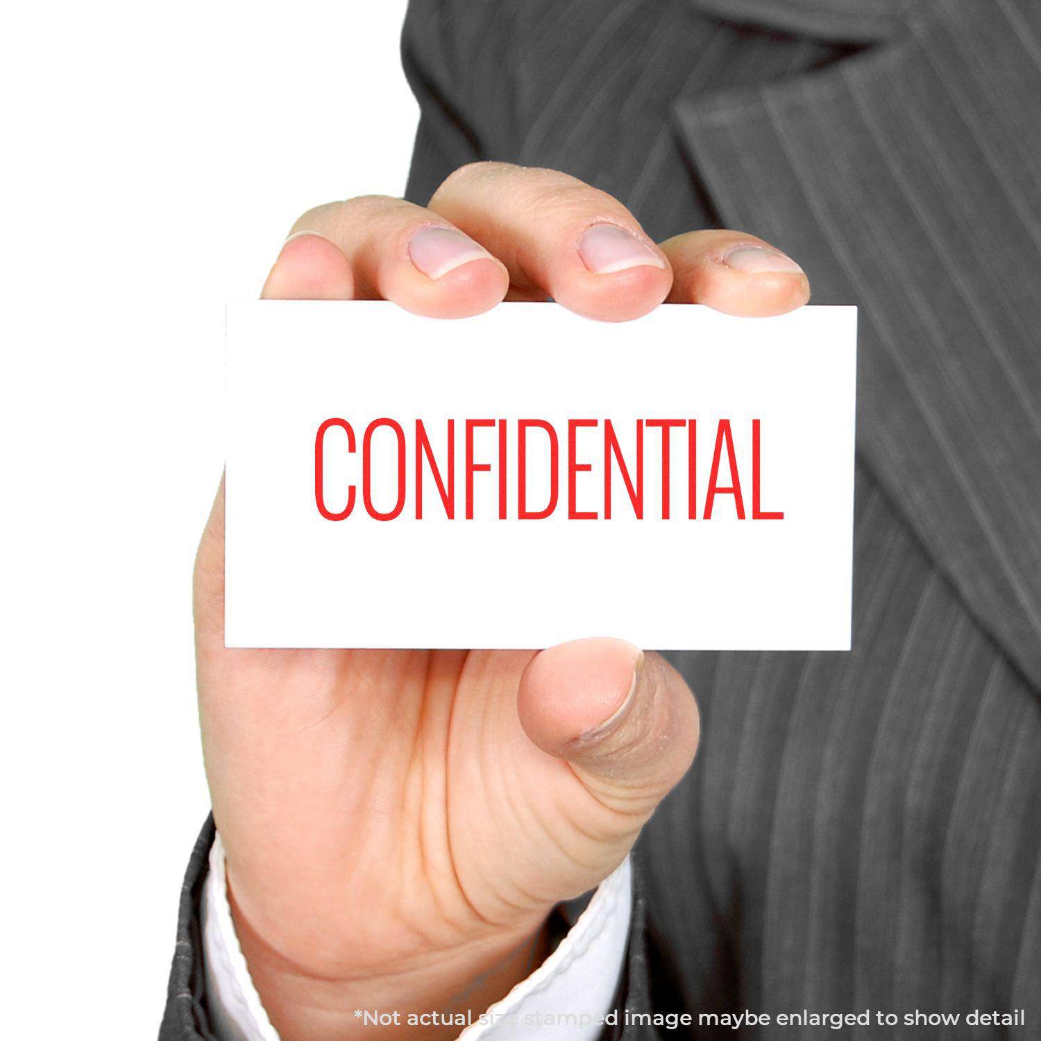 A hand holding a card stamped with CONFIDENTIAL in red using the Large Pre-Inked Narrow Font Confidential Stamp.