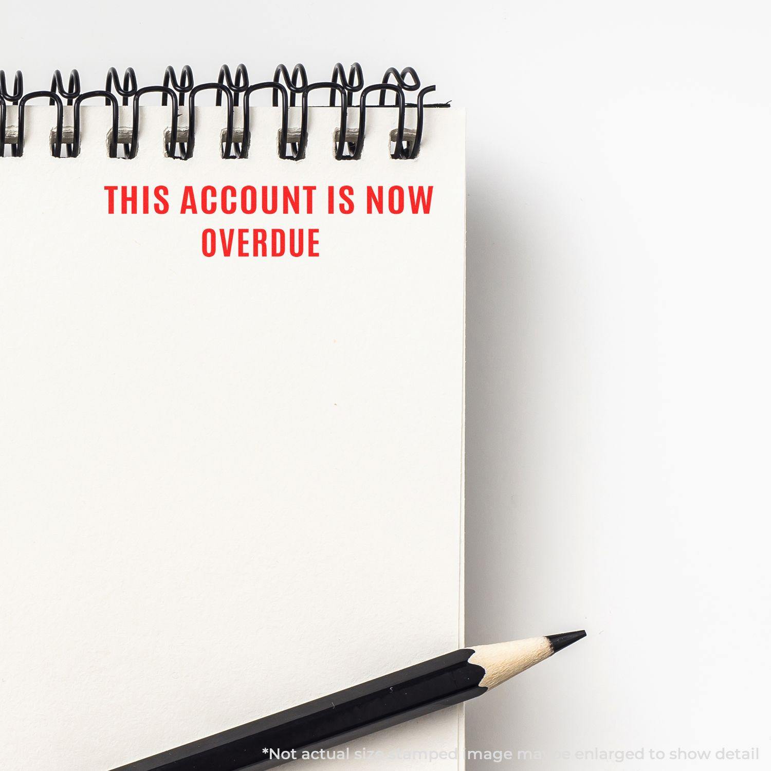 Narrow This Account Is Now Overdue rubber stamp impression on a spiral notebook page with a pencil beside it.