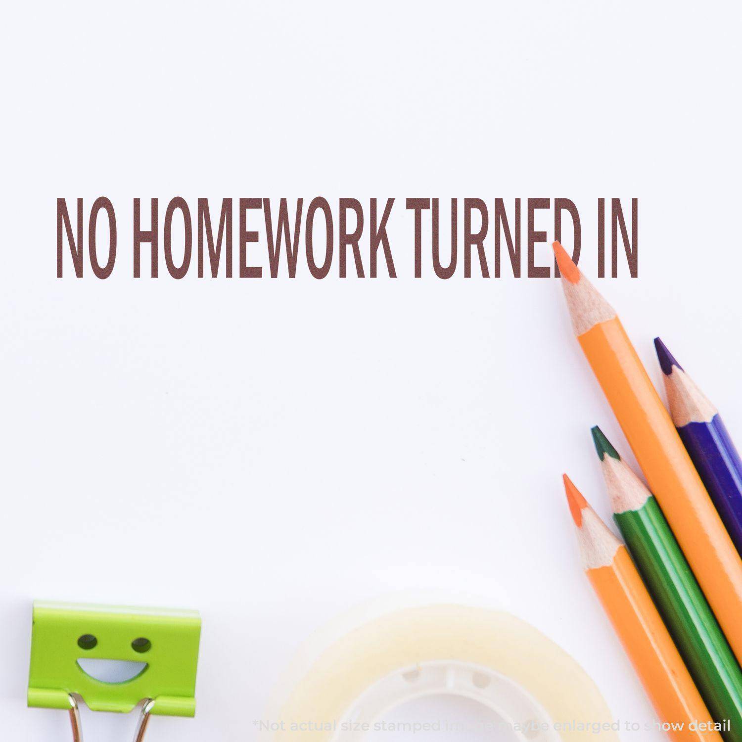 Large Pre-Inked No Homework Turned In Stamp impression on paper with colored pencils, a smiling binder clip, and tape in the background.