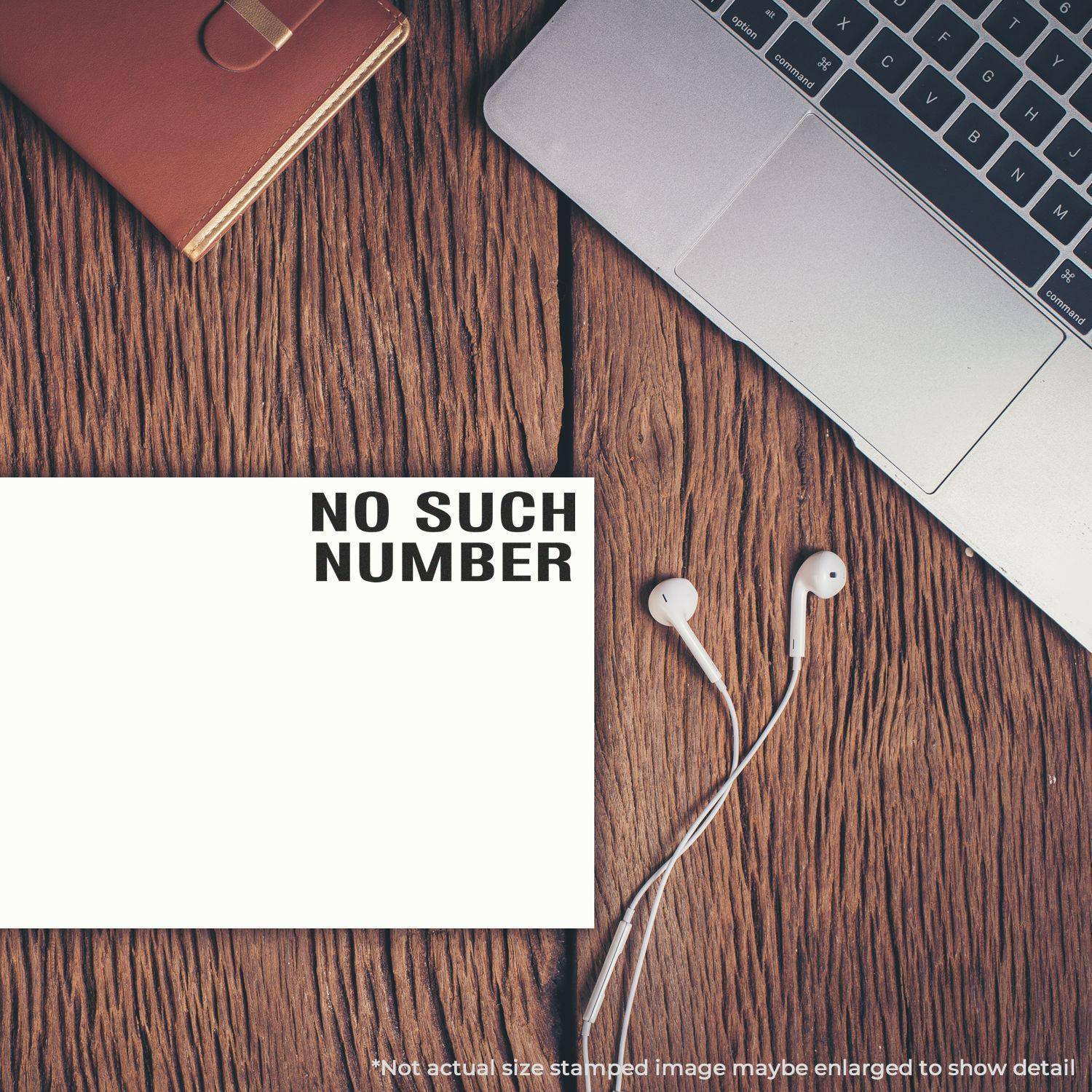 Large Pre-Inked No Such Number Stamp used on paper, placed on a wooden desk next to a laptop, earphones, and a notebook.