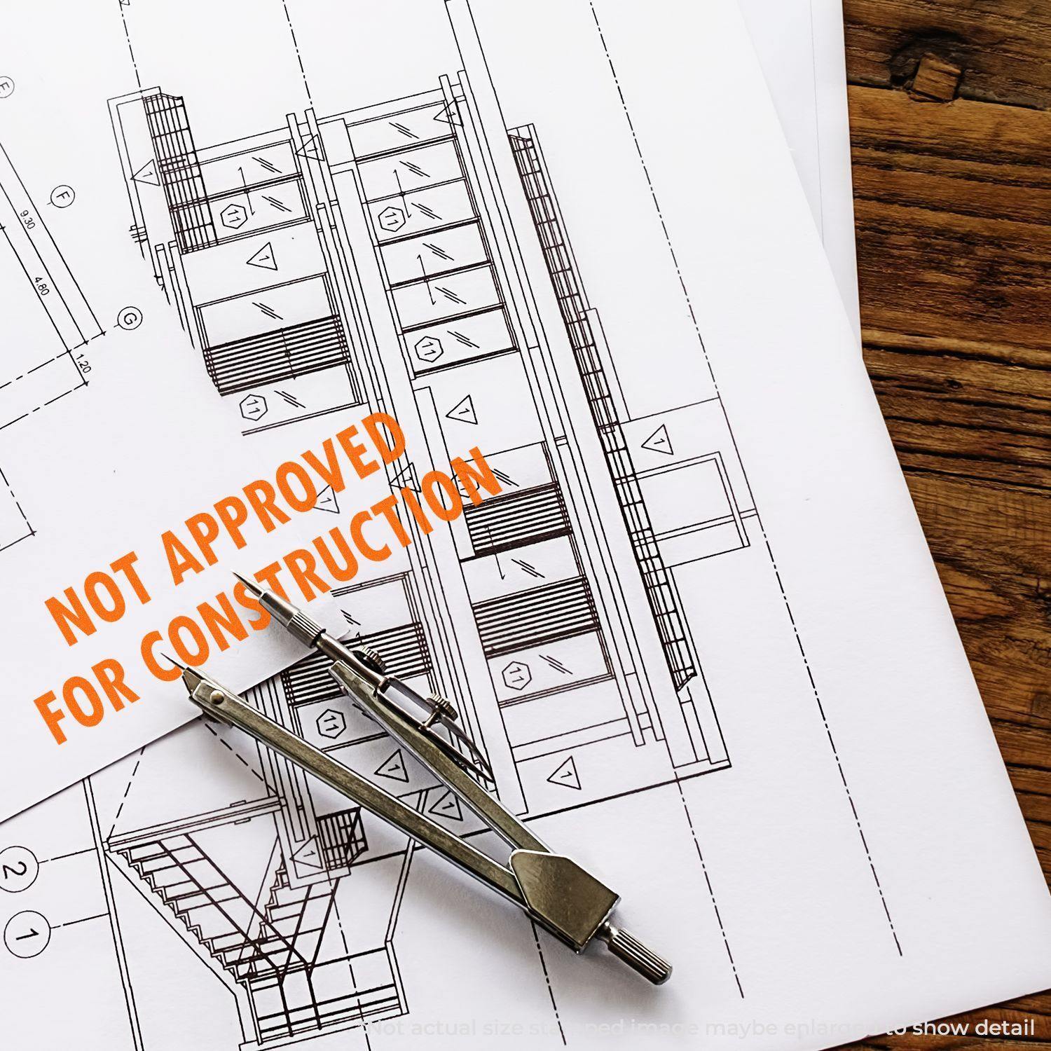 Slim Pre-Inked Not Approved For Construction Stamp on architectural blueprints with a compass tool on a wooden table.