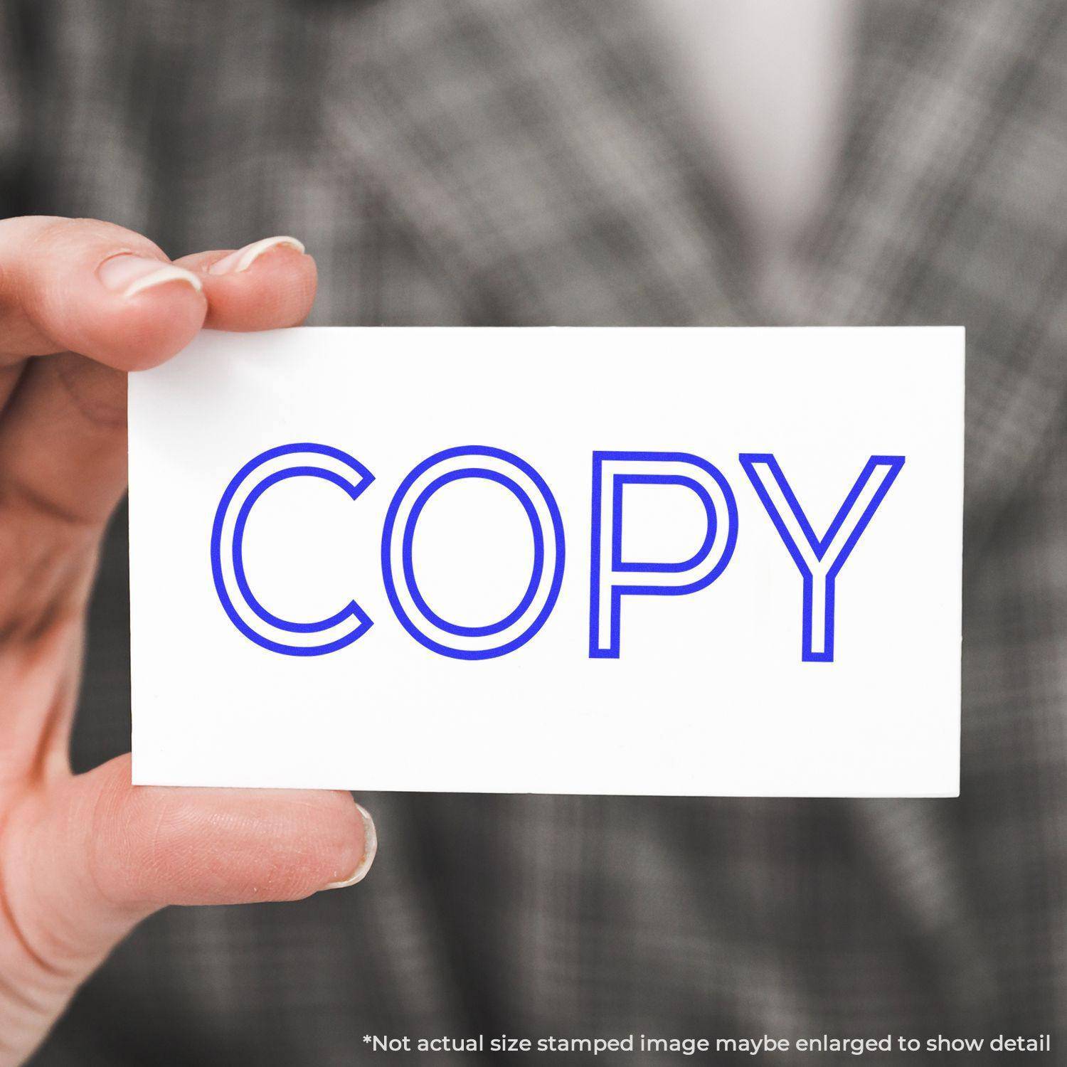 Person holding a white card stamped with COPY in blue using the Large Pre-Inked Outline Copy Stamp.