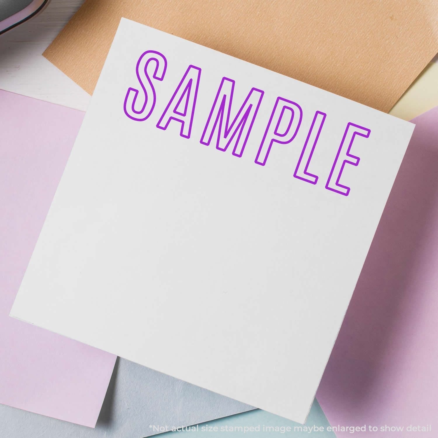 A white paper stamped with SAMPLE in purple ink using the Self Inking Outline Sample Stamp, placed on a pastel-colored background.