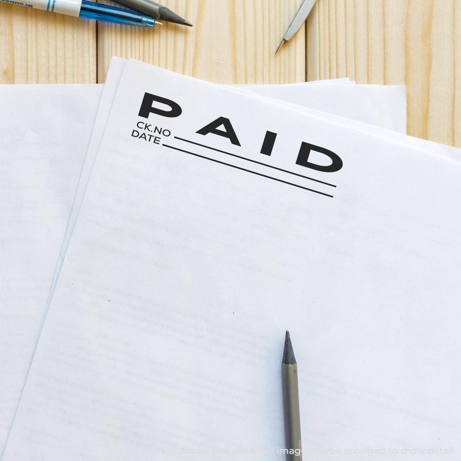 Large Pre-Inked Paid with Ck No Stamp used on a document, with pens and papers on a wooden surface.