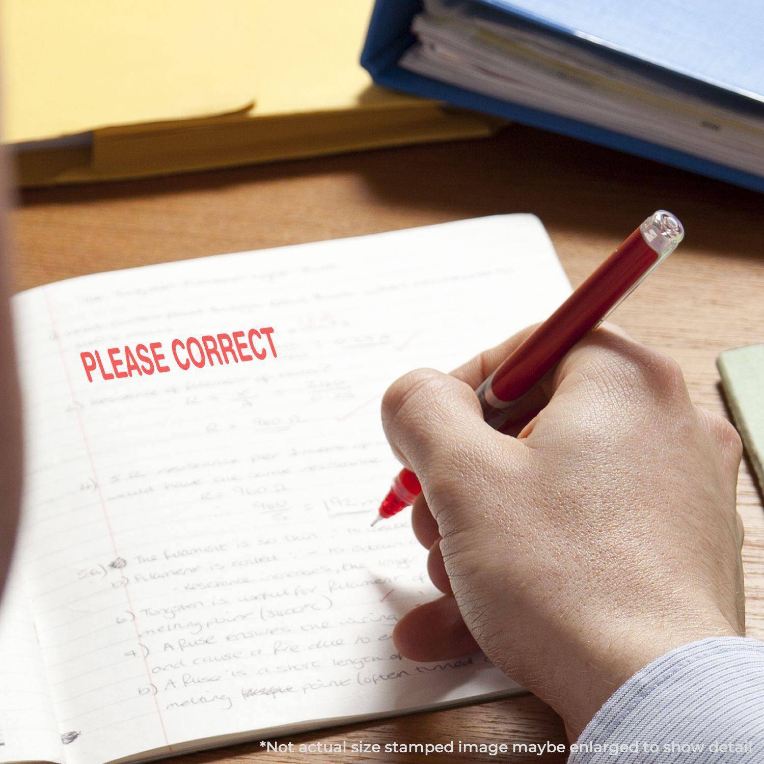 A hand holding a pen next to a notebook with PLEASE CORRECT stamped in red using the Large Pre-Inked Please Correct Stamp.
