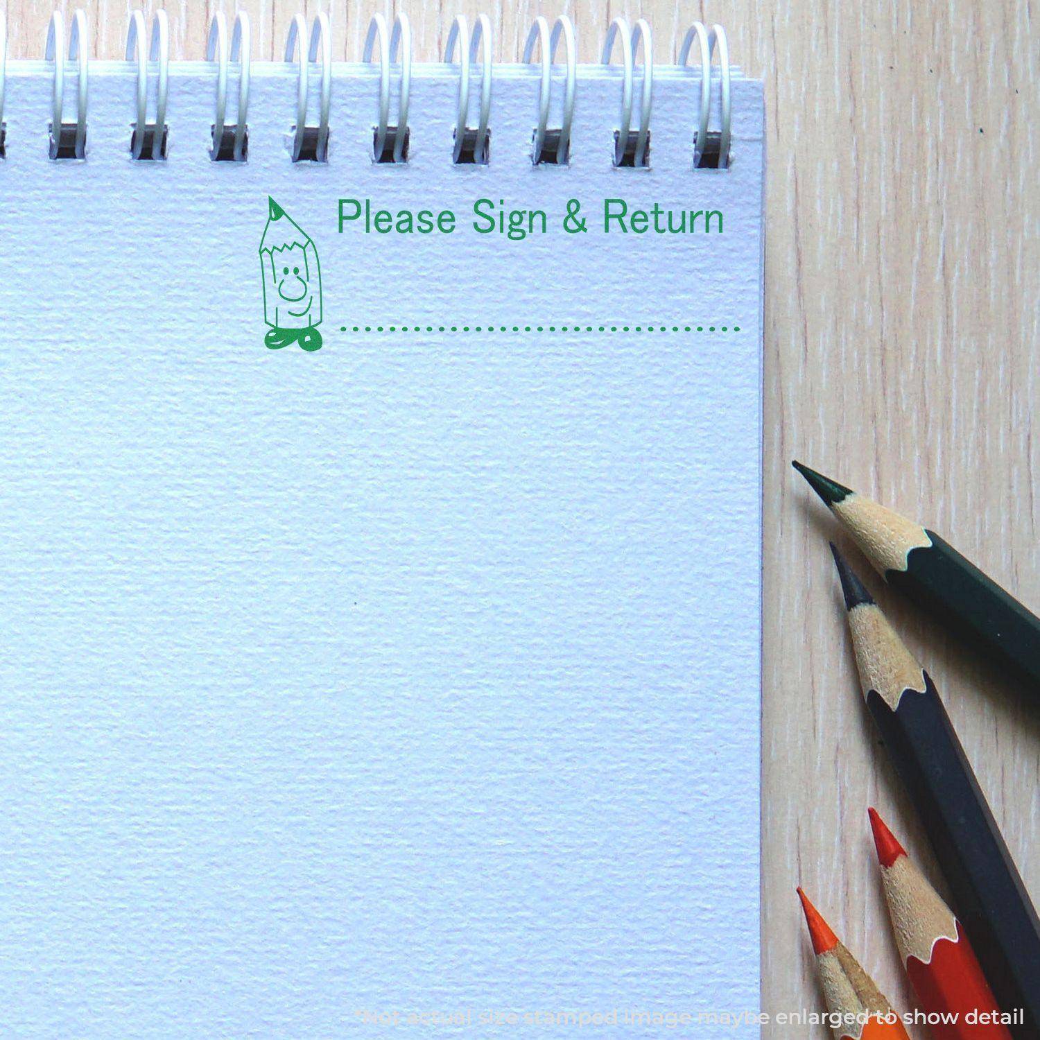 Large Pre-Inked Please Sign and Return Stamp in green ink on a spiral notebook page with colored pencils beside it.