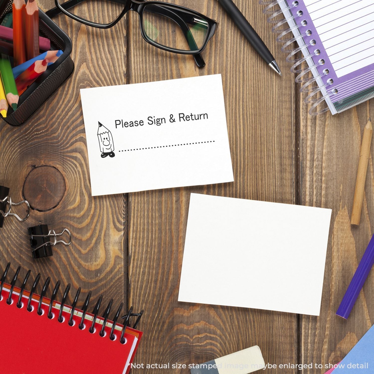 Self Inking Please Sign and Return Stamp on a card, surrounded by office supplies like notebooks, glasses, and pens on a wooden desk.