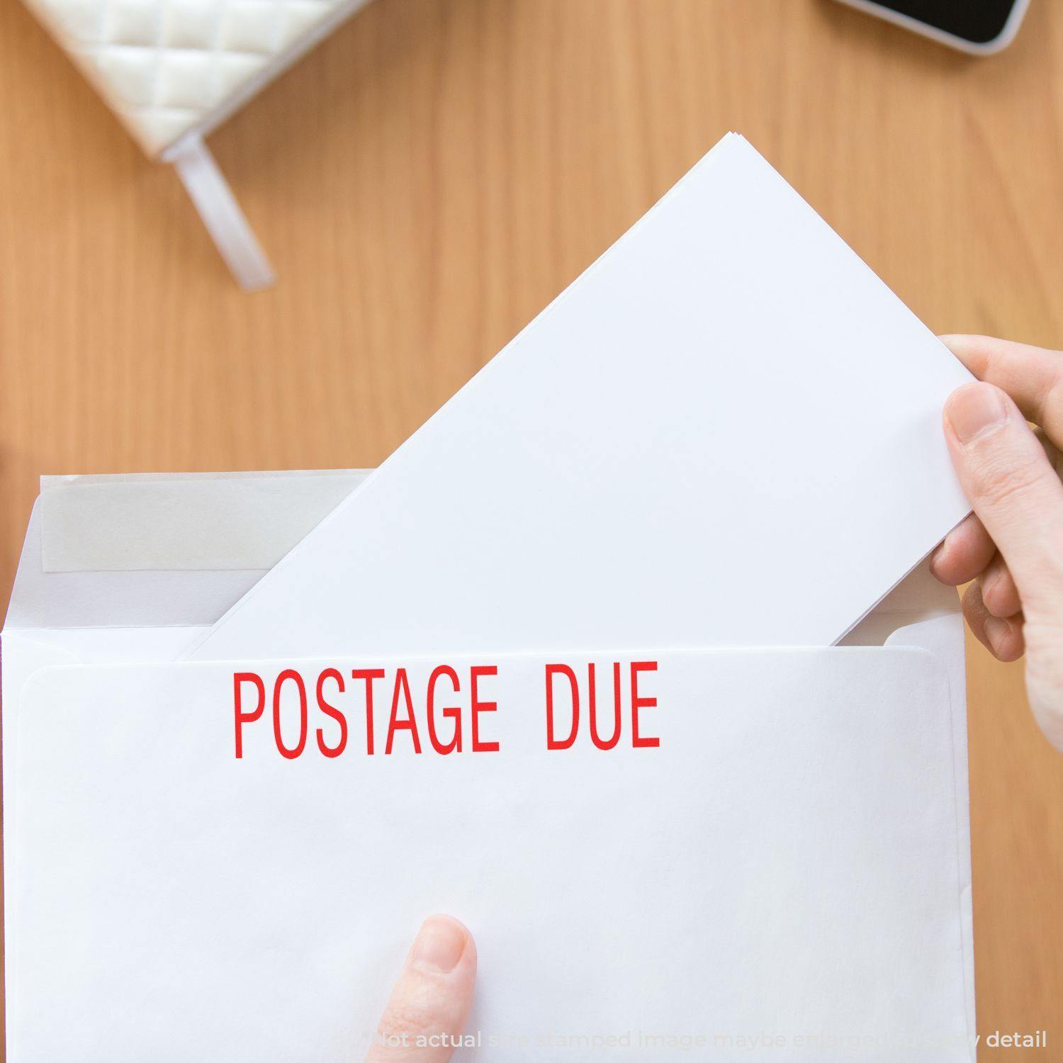 Person holding an envelope with a POSTAGE DUE Slim Pre-Inked Postage Due Stamp marking in red on the front.