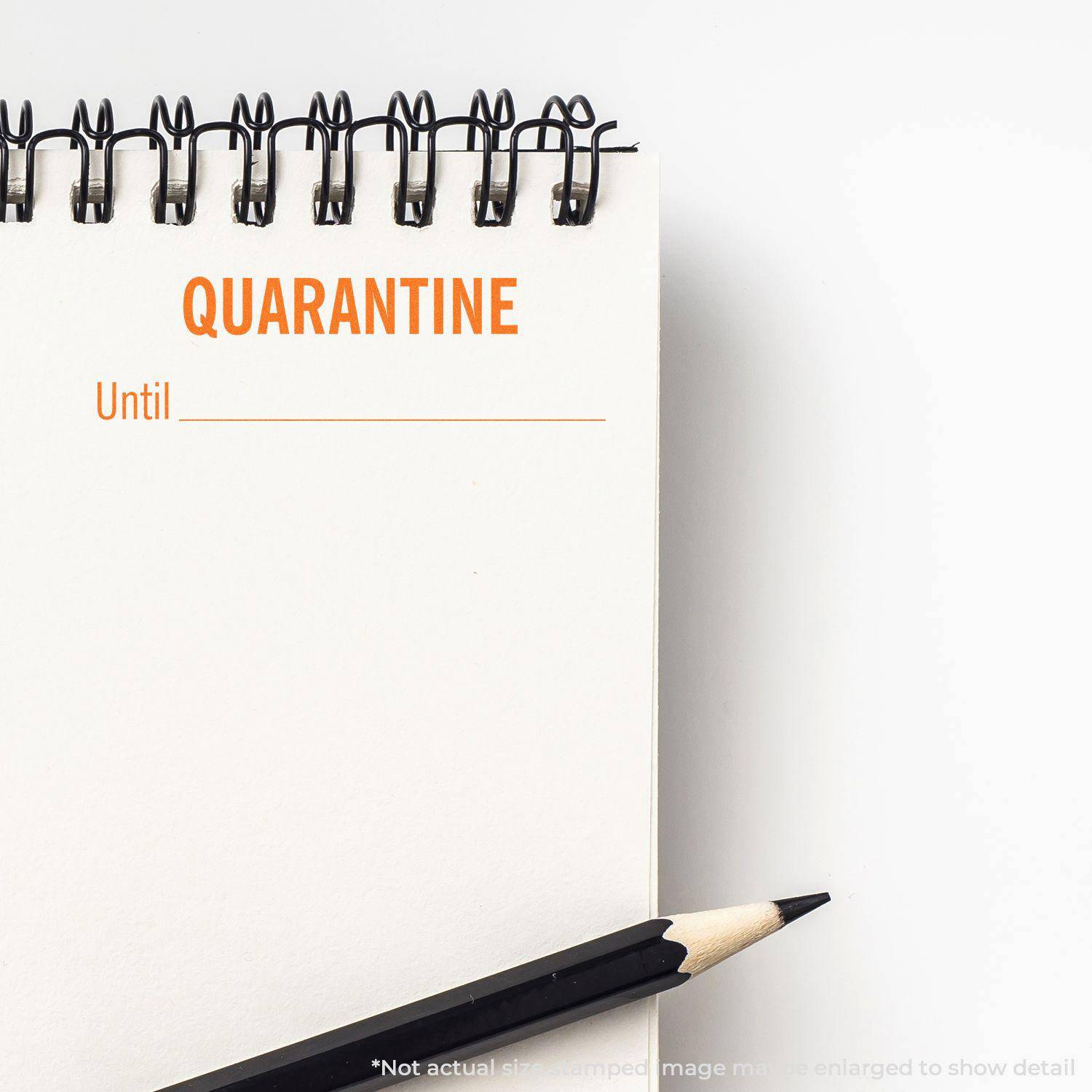 Large Pre-Inked Quarantine Until Stamp in use on a spiral notebook with a pencil beside it. The stamp reads QUARANTINE Until _______ .