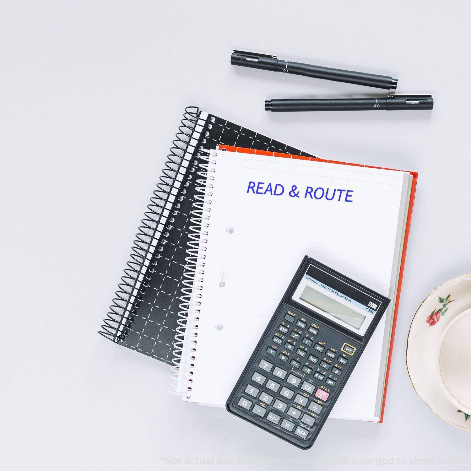 Large Read & Route Rubber Stamp used on a notebook page, with a calculator, pens, and a teacup on a white desk.