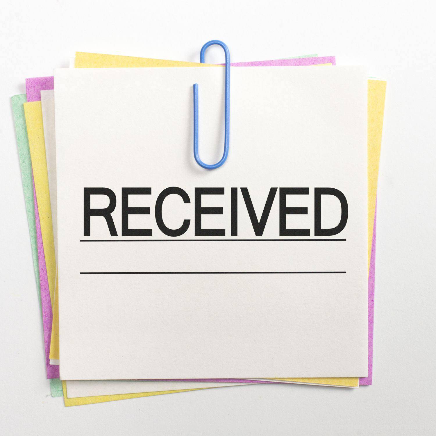 Large Pre-Inked Received with Line Stamp marking a stack of papers, secured with a blue paperclip, on a white background.