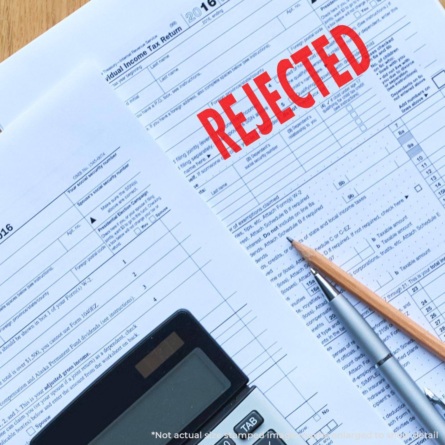 Tax forms stamped with a Large Rejected Rubber Stamp in red ink, alongside a calculator, pen, and pencil on a blue background.